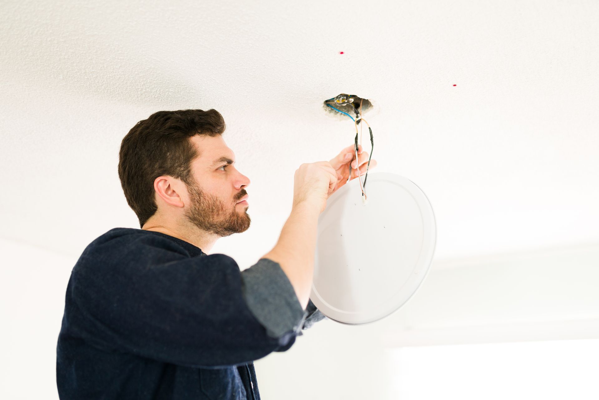 A man is fixing a light fixture on the ceiling.