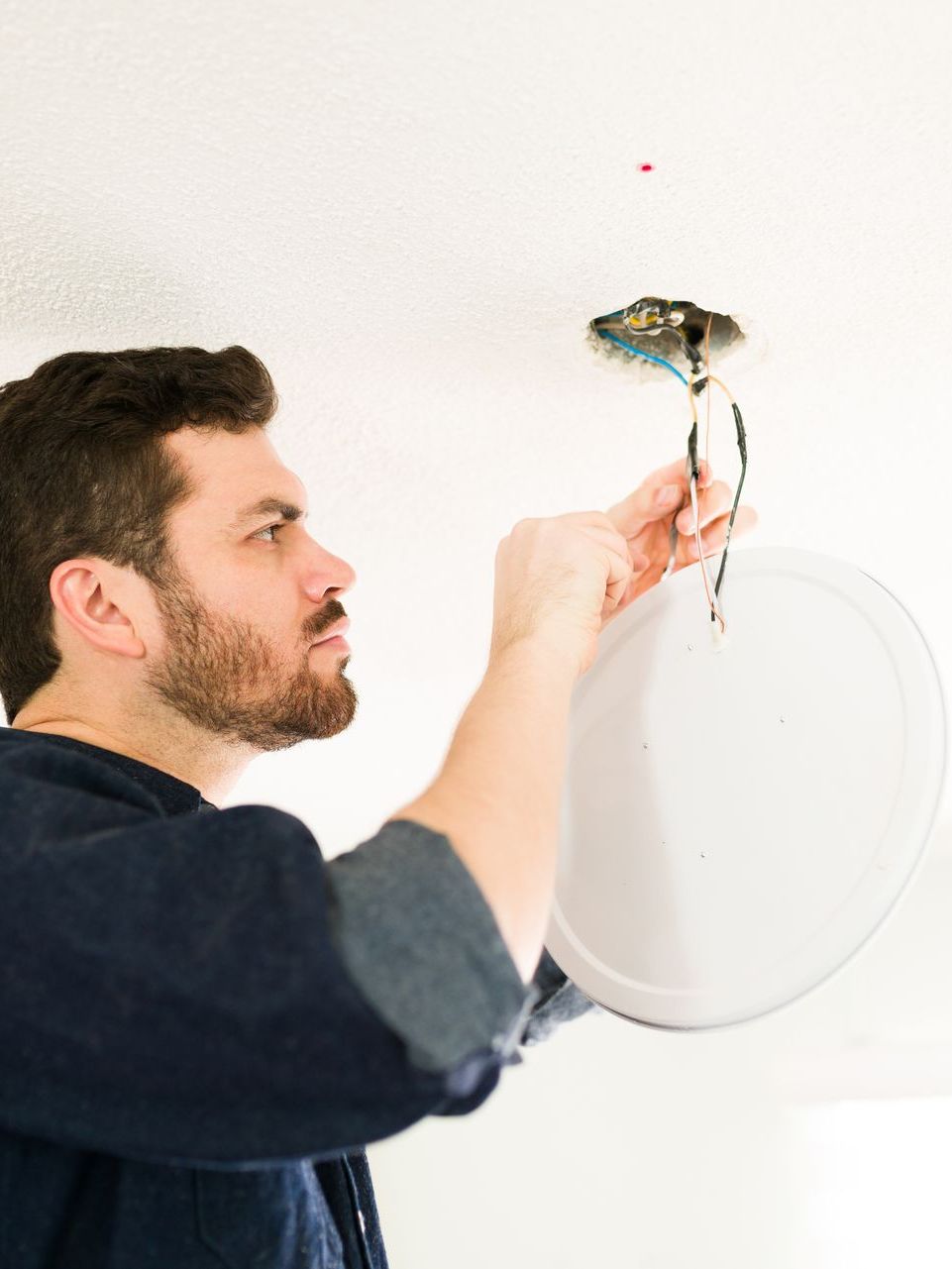 A man is fixing a light fixture on the ceiling.