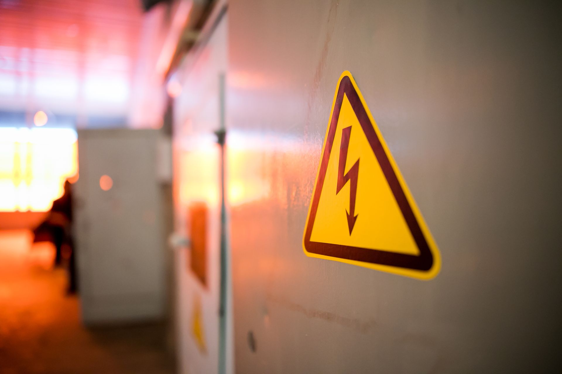 Yellow electrical hazard sign on a metal cabinet in a dimly lit industrial setting.