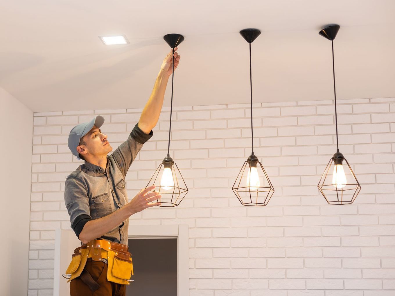 A man is hanging a light from the ceiling in a room.