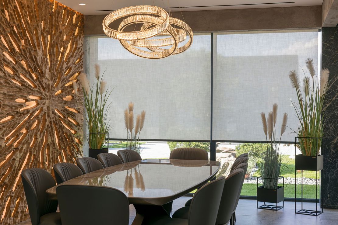 A dining room with a long table and chairs and a chandelier hanging from the ceiling.