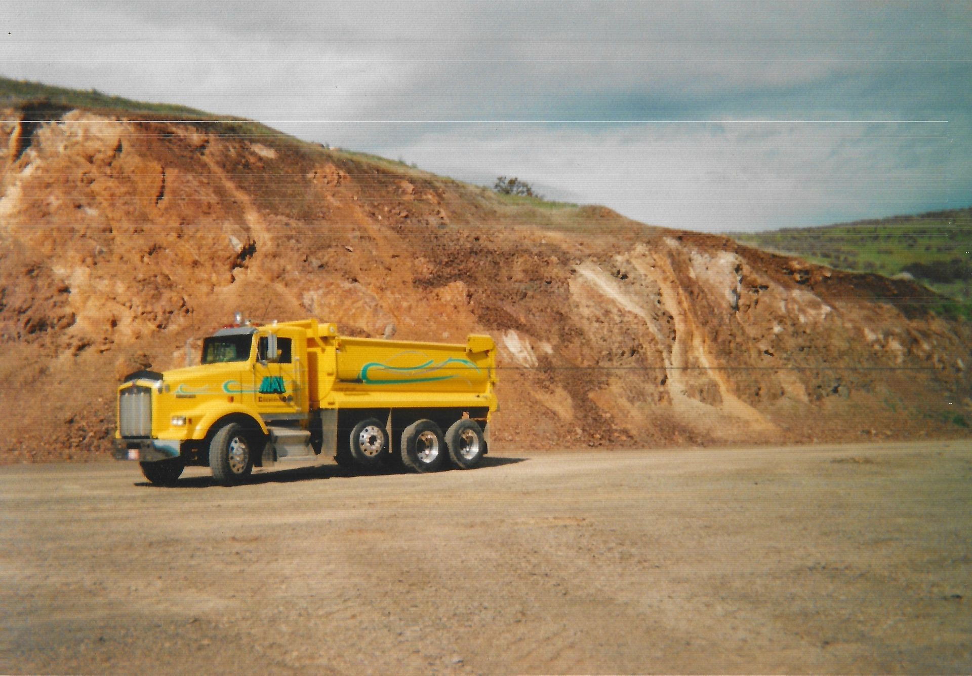 A yellow dump truck is driving down a dirt road in Ashland, Oregon.