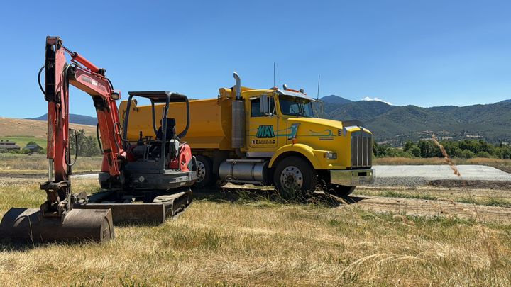 A mini excavator and a big yellow dump truck on a home construction site, building a house pad in Ashland, Oregon.