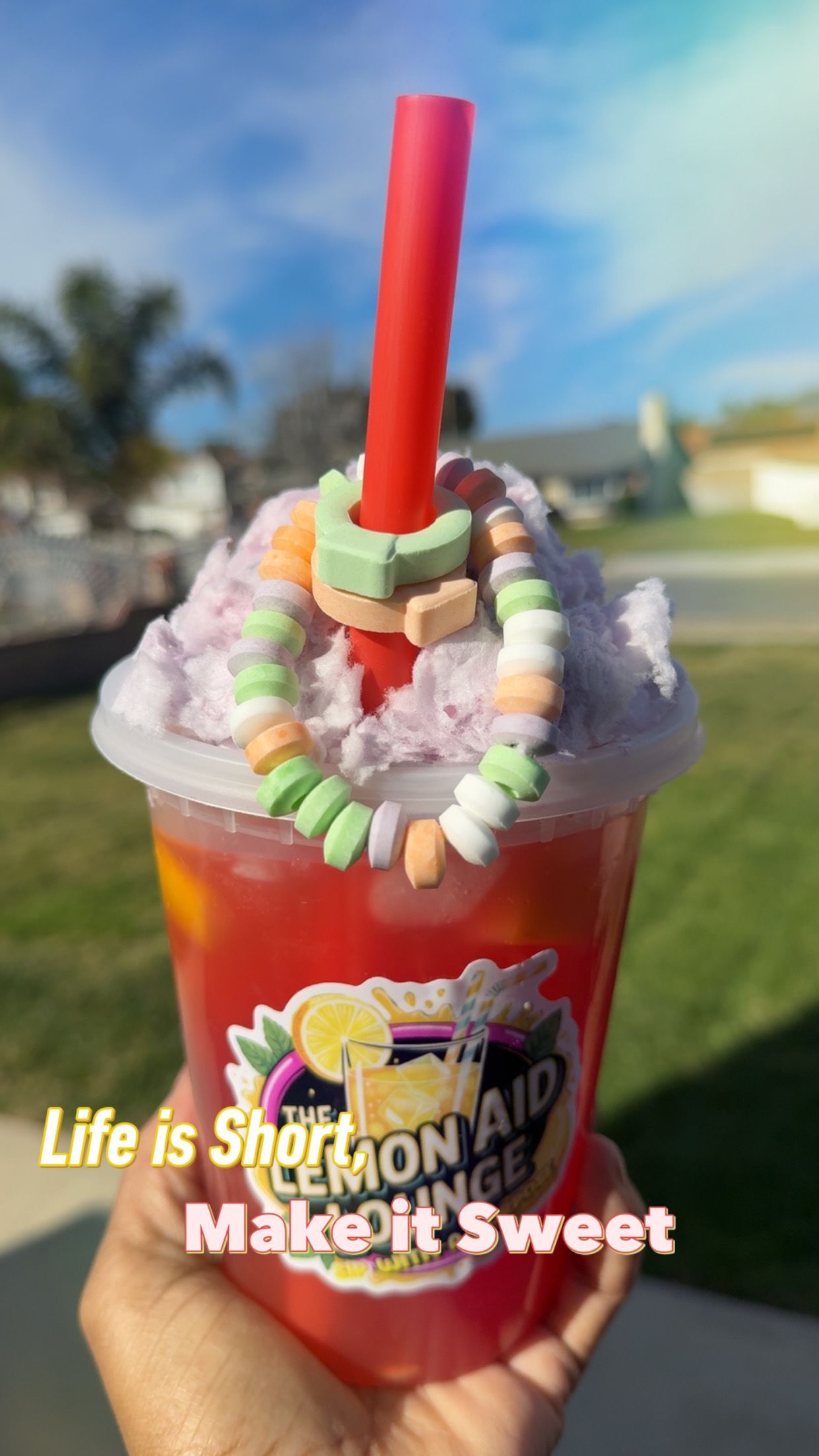 Hand holding a clear cup with green lemonade and a straw, labeled “Lemonade Lounge.”
