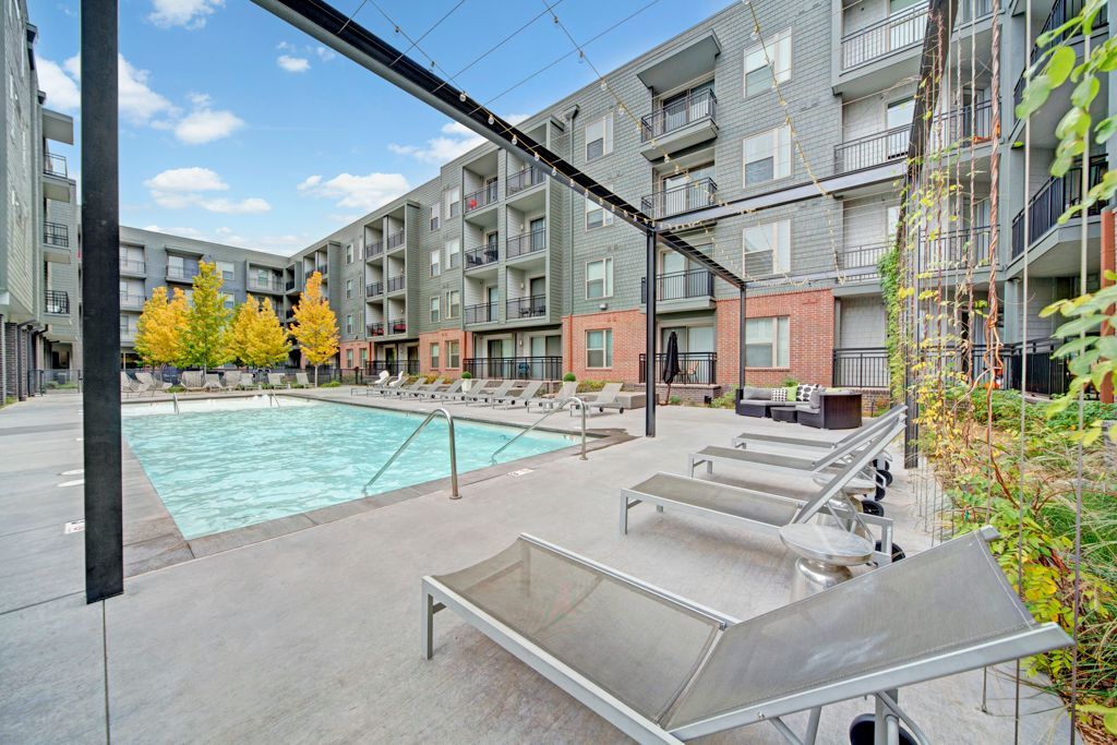 A large apartment building with a swimming pool and lounge chairs in front of it.