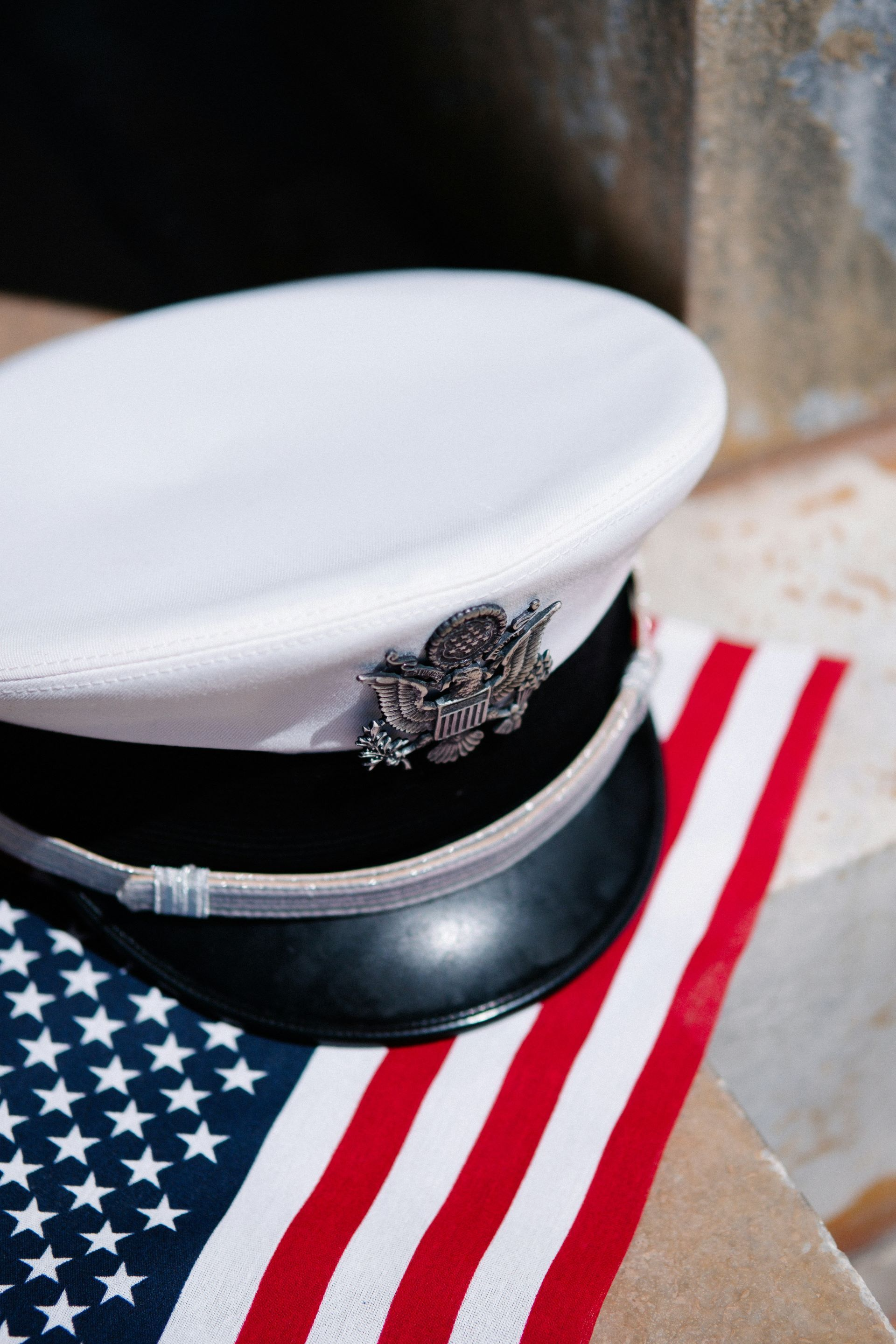 White naval hat with insignia atop an American flag. The flag’s red and white stripes are visible.