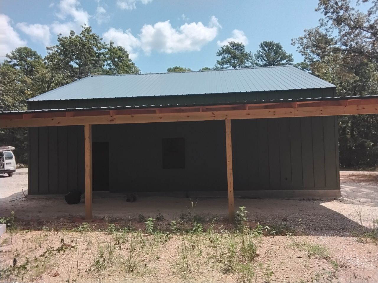 Green metal-sided building with a covered porch, in a wooded area.