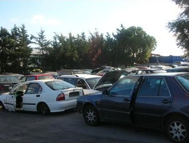 Un mucchio di auto distrutte, di vari colori, ammassate in uno sfasciacarrozze.