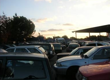 Un'auto bianca viene trainata da un carro attrezzi su una strada; la rampa è abbassata.