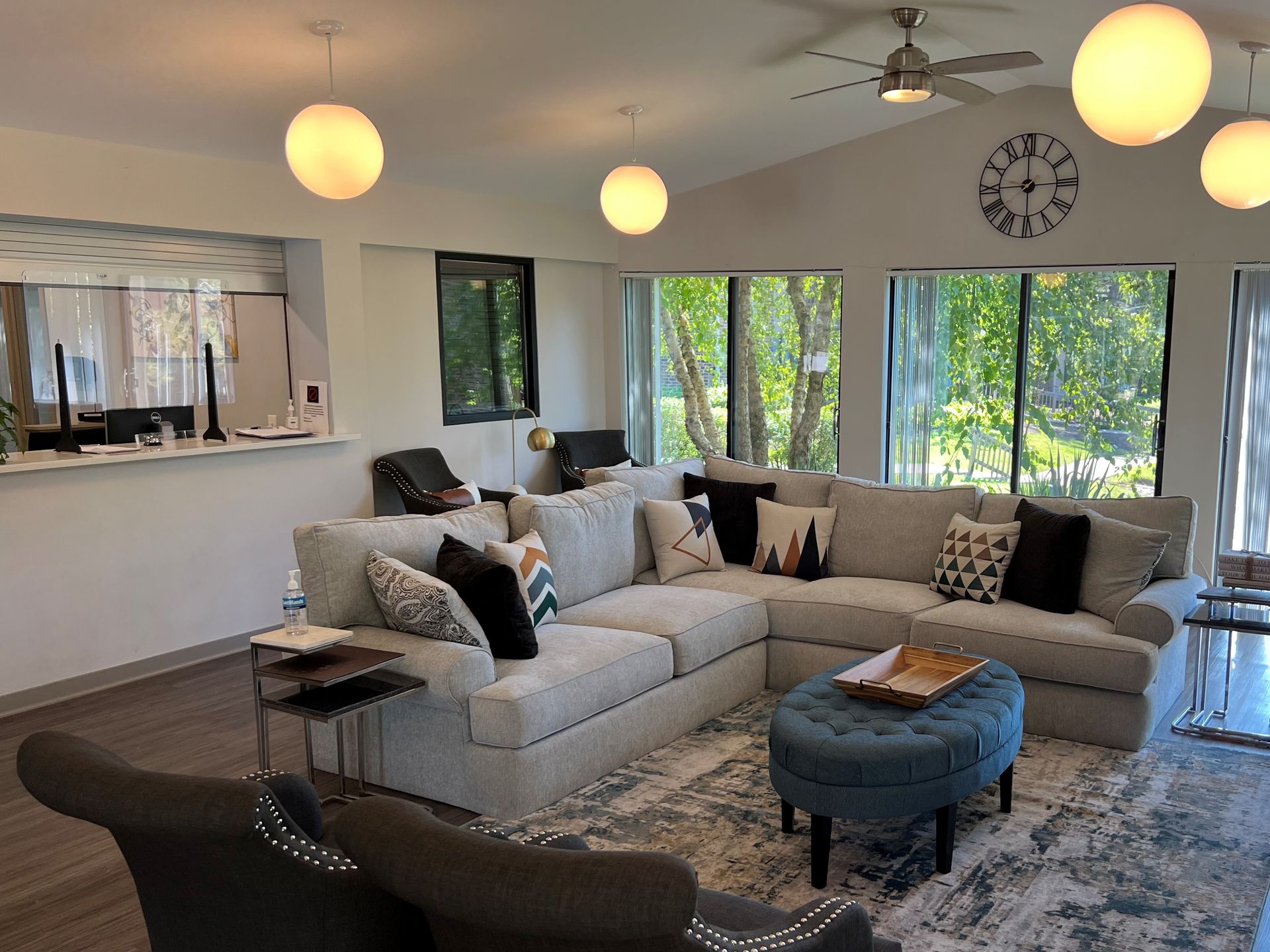 Living room with a gray sectional sofa, round ottoman, large windows, and globe pendant lights.