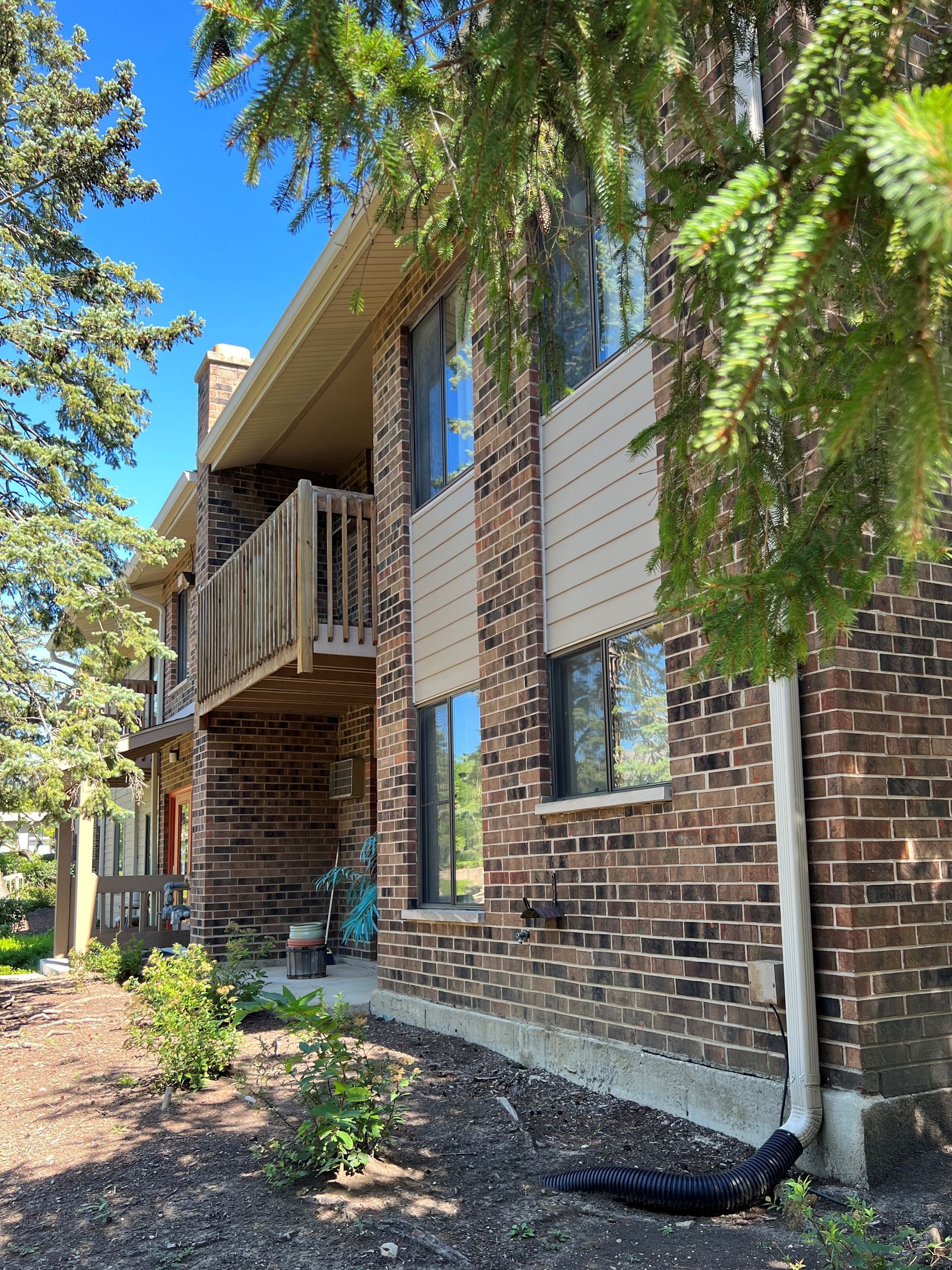 Two-story brick building with a wooden balcony and tan siding. Trees frame the building.