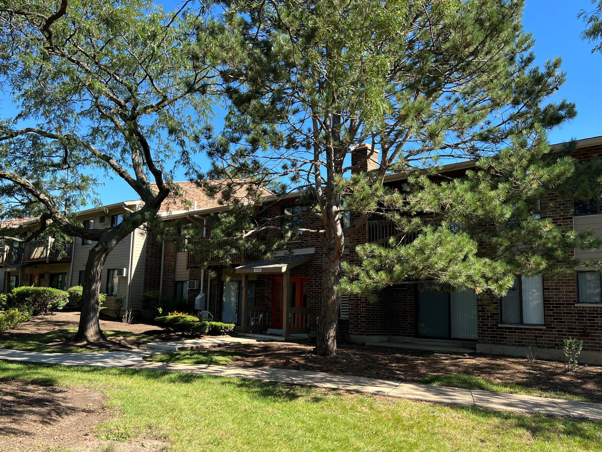 Apartment building exterior, two stories, with trees in front; blue sky visible.