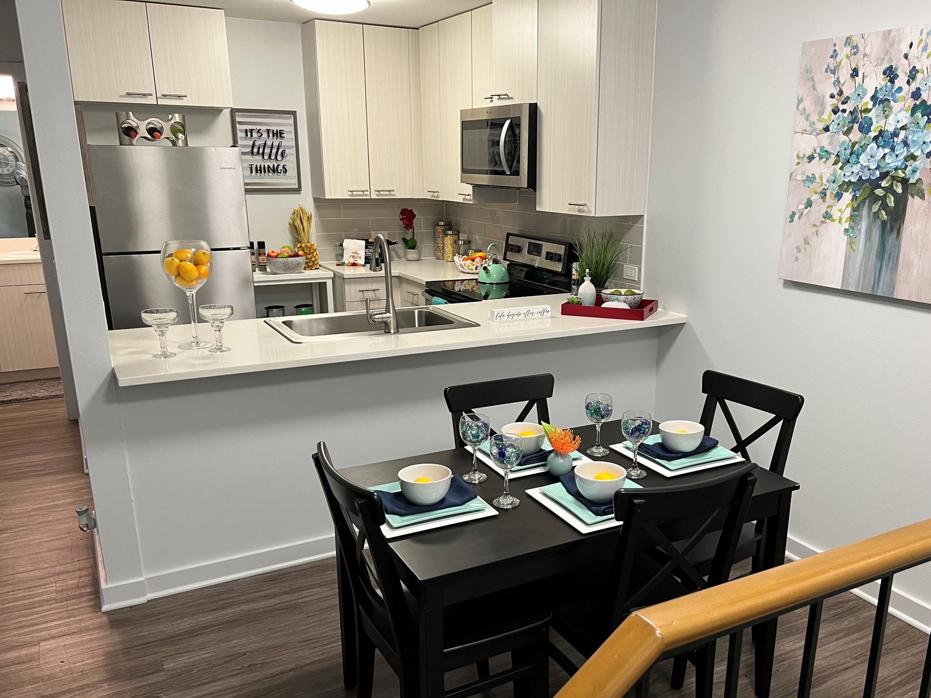 Kitchen and dining area with a table set for four, featuring light cabinets and a painting.