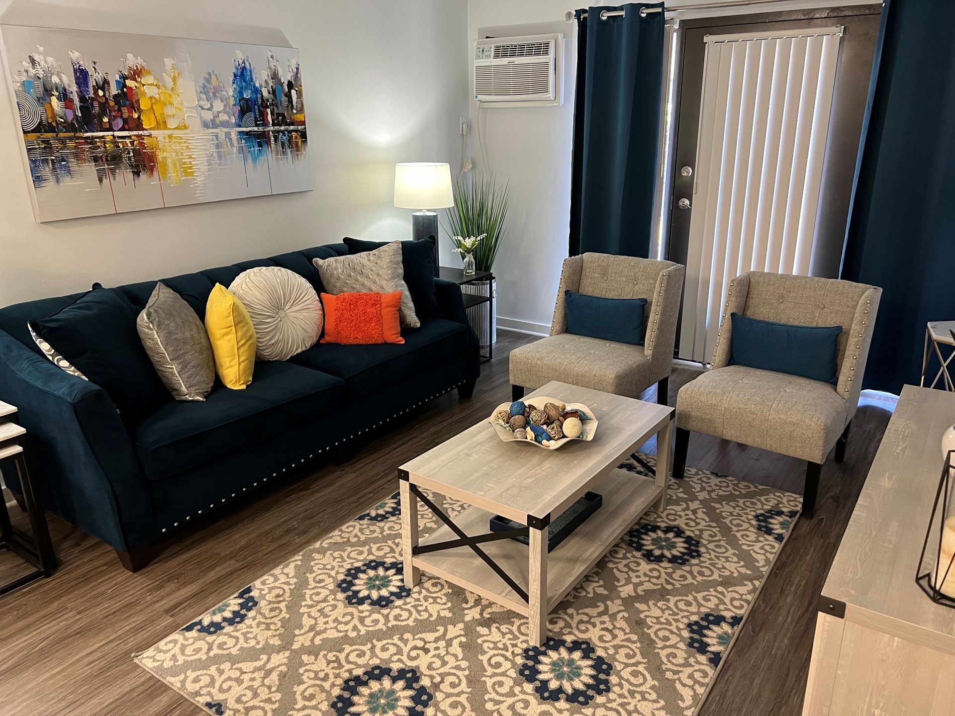 Living room with blue sofa, two chairs, coffee table, rug, artwork, and curtains.