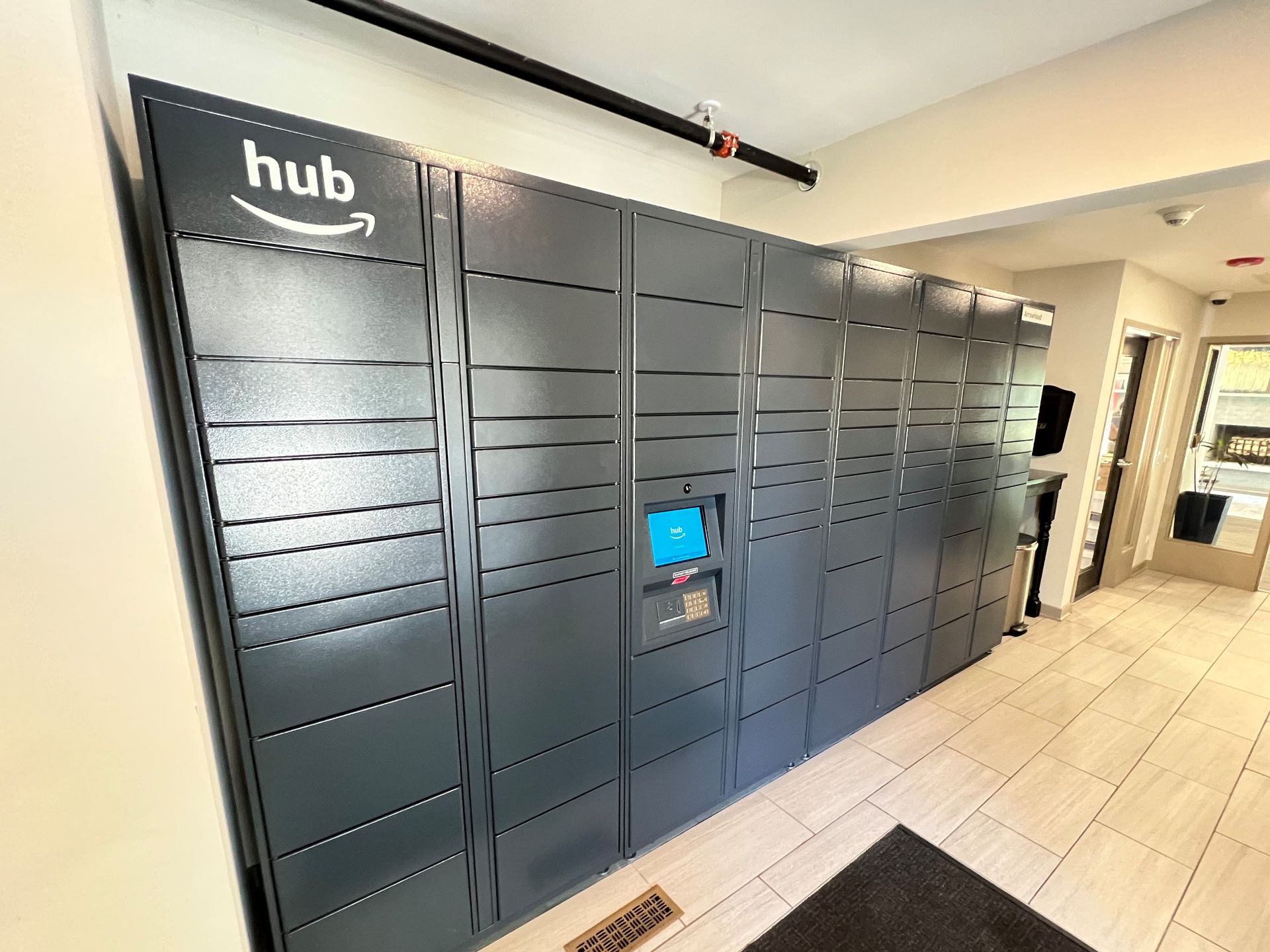 Amazon Hub locker system in an apartment hallway. Dark gray lockers with a touchscreen.