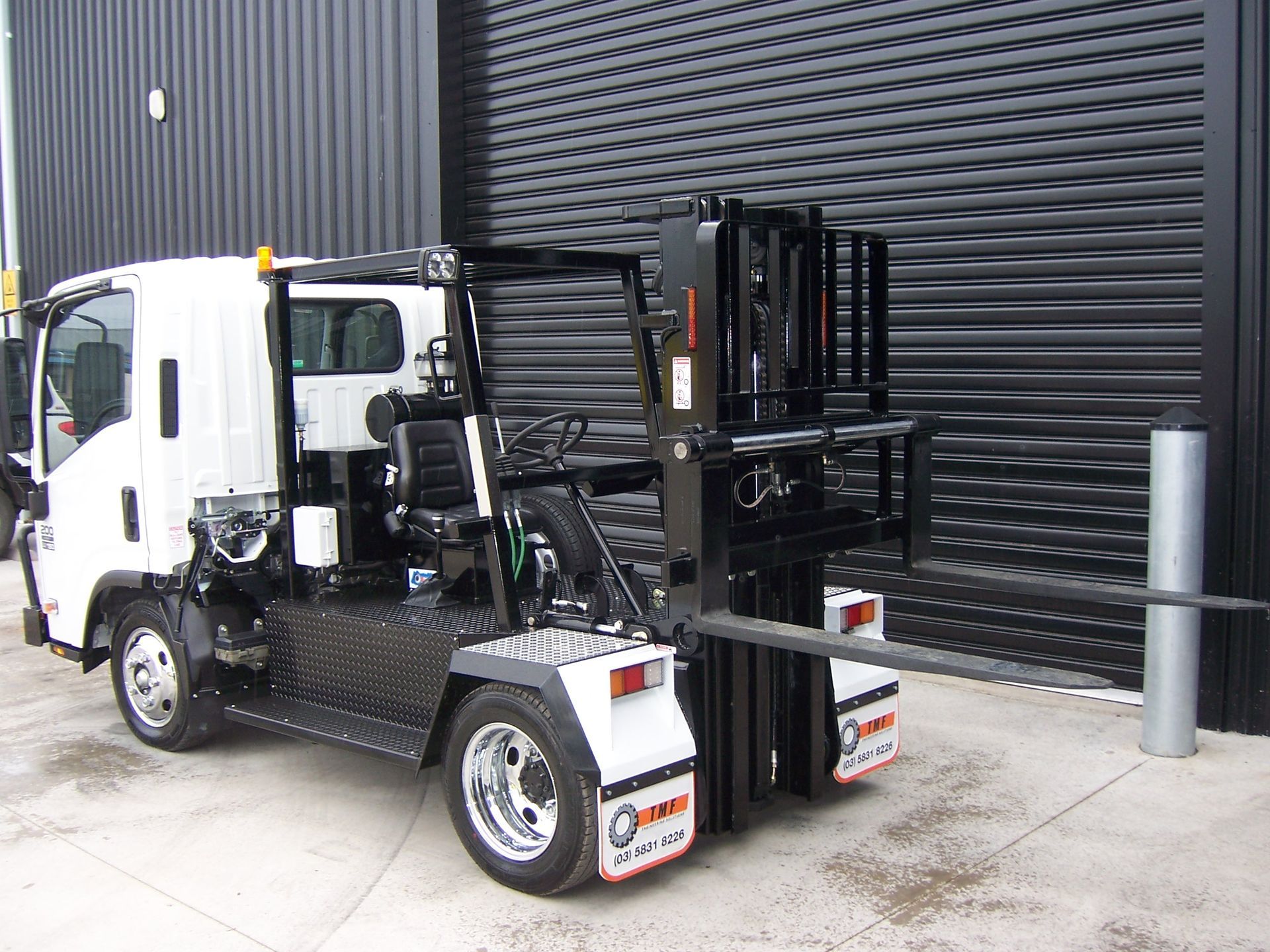 A white truck with a forklift attached to it is parked in front of a building — TMF Engineering In Benalla, VIC