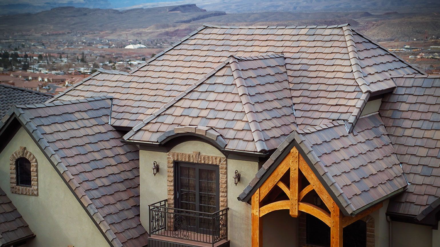 Brown tile roof on a luxury home with a wooden portico. Background shows a mountainous landscape.
