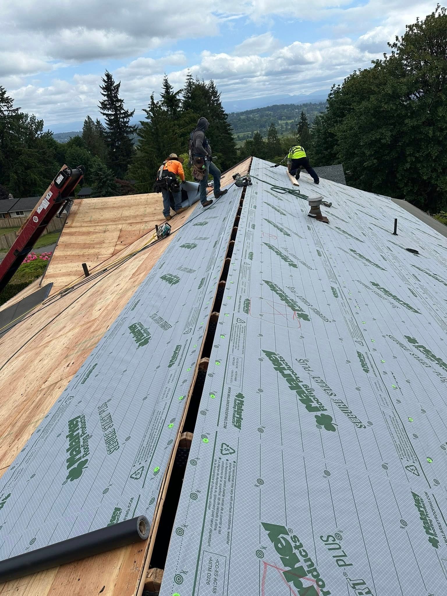Construction workers installing roof underlayment on a sloped roof, with a scenic outdoor view.