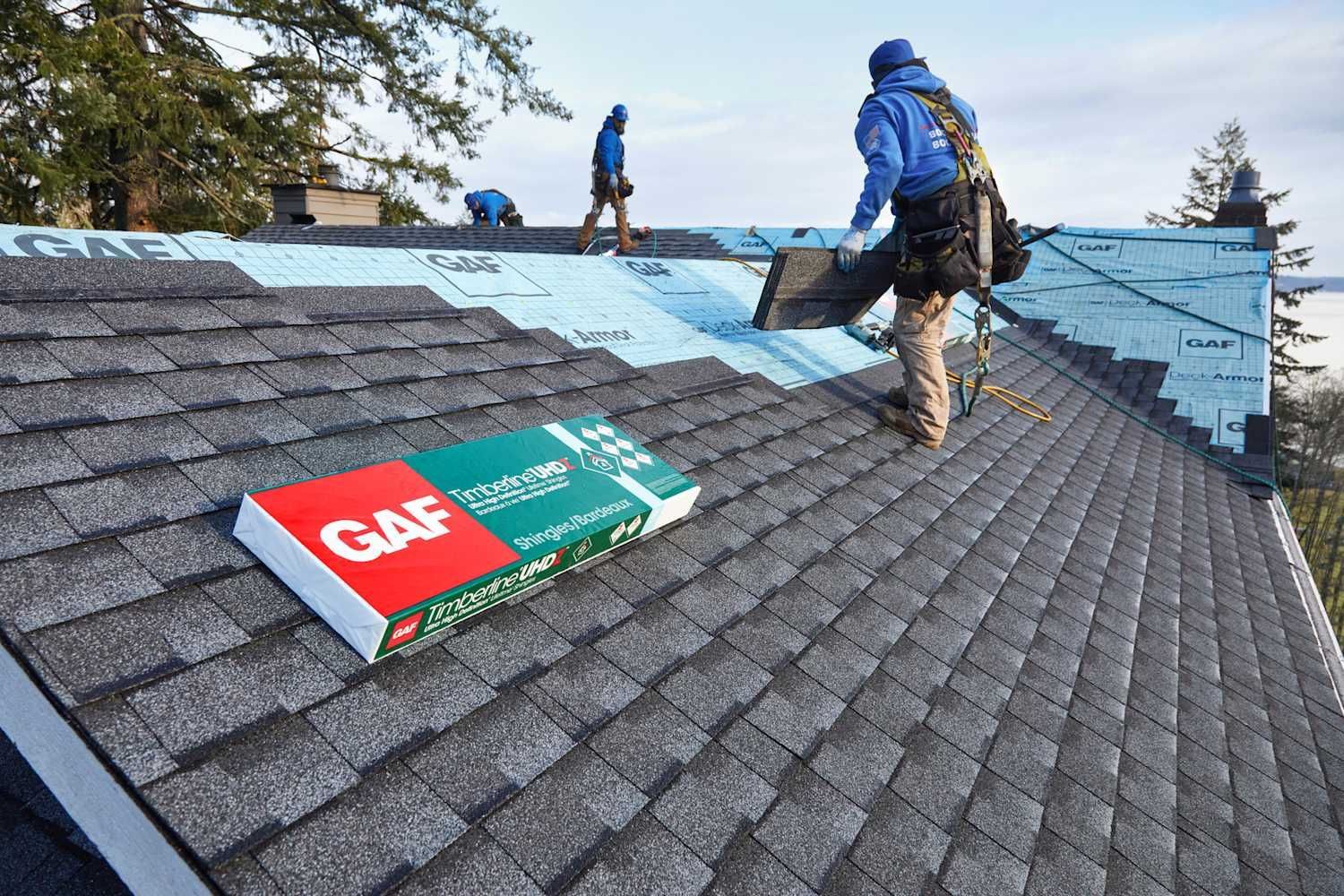 Roofers installing shingles on a house roof. GAF shingle box in foreground.