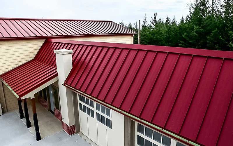 Red metal roof on a building with white garage doors and a beige chimney.