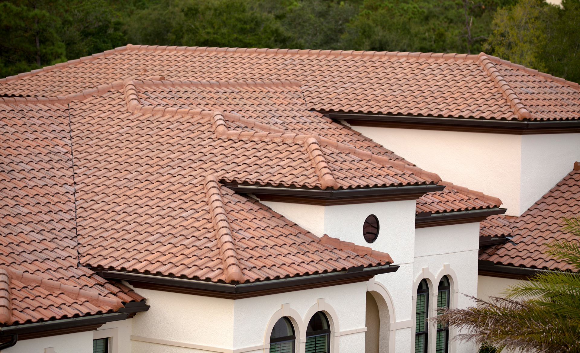 Clay tile roof on a cream-colored house with arched windows.