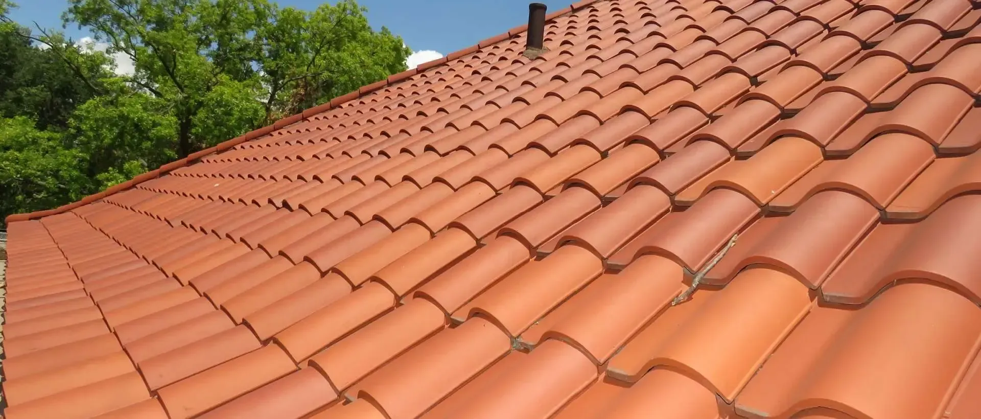 Red clay tile roof with a chimney and green trees in the background.