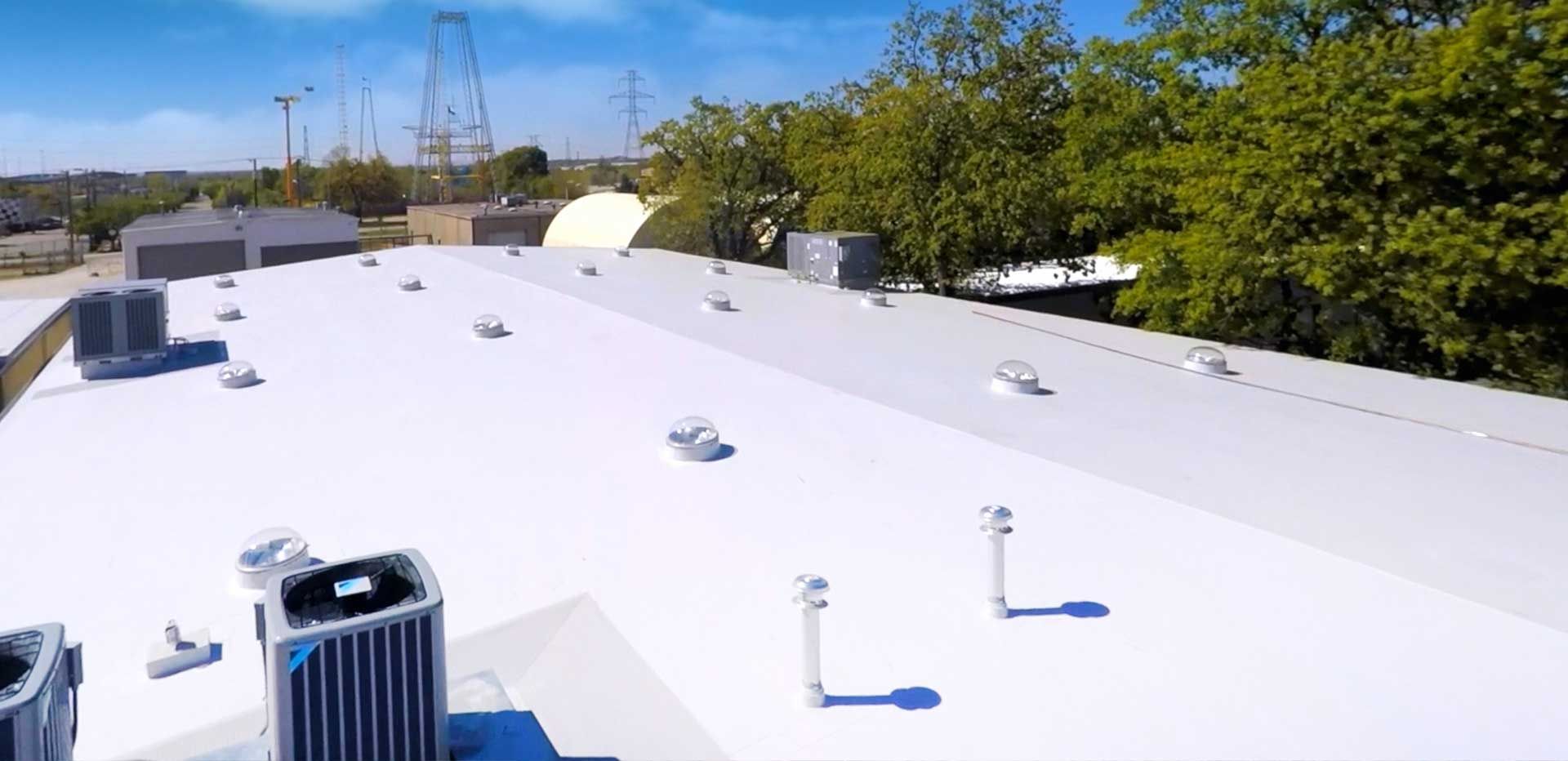 A white roof with HVAC units, vents, and trees. Power lines in the background under a blue sky.