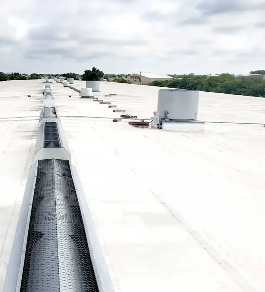 White commercial flat roof with HVAC units and a long ventilation structure. Overcast sky.