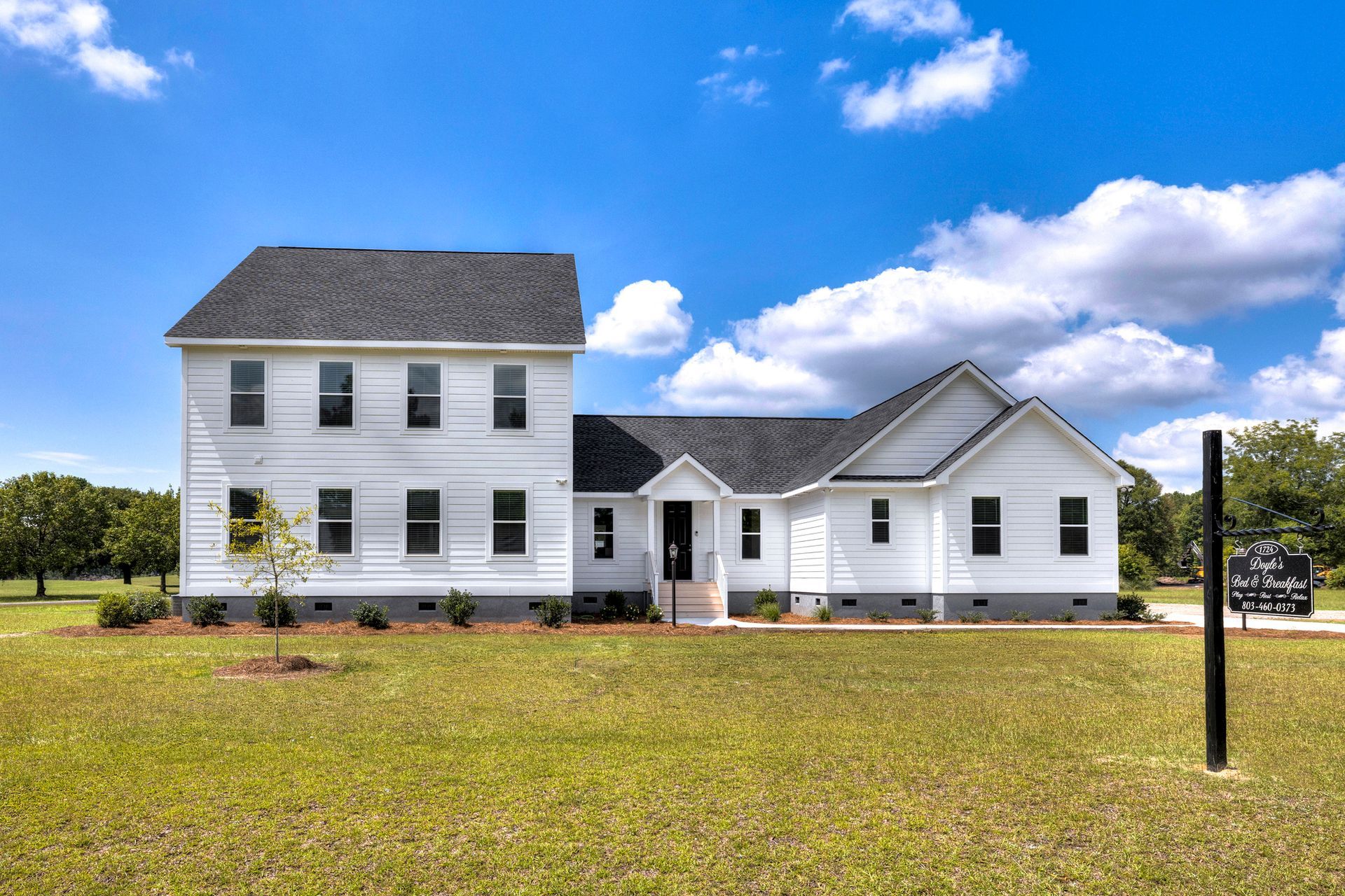 White two-story house with dark roof and windows, set against a blue sky with clouds and green lawn.