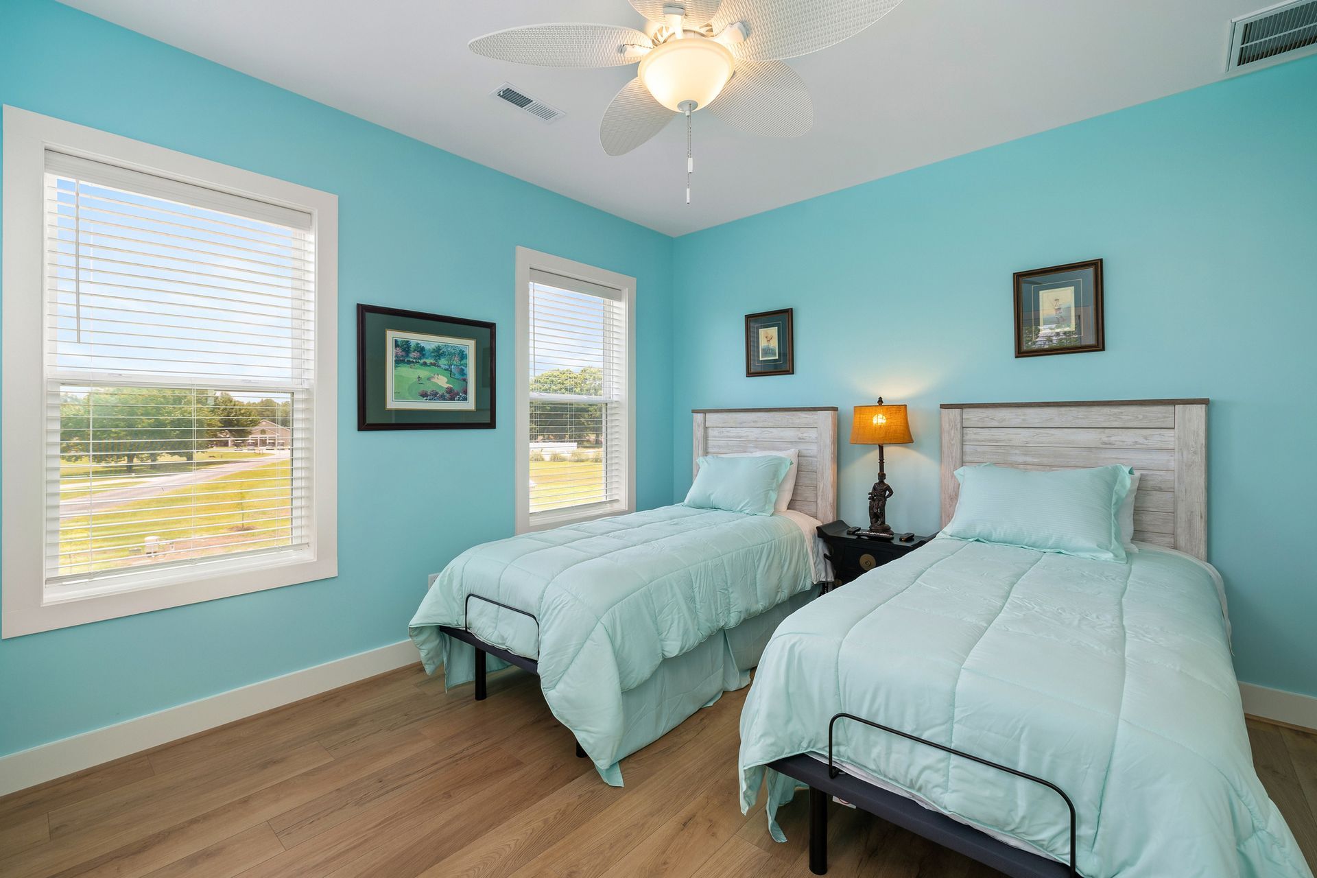 Bedroom with two twin beds, turquoise walls, two windows, and light wooden floor.