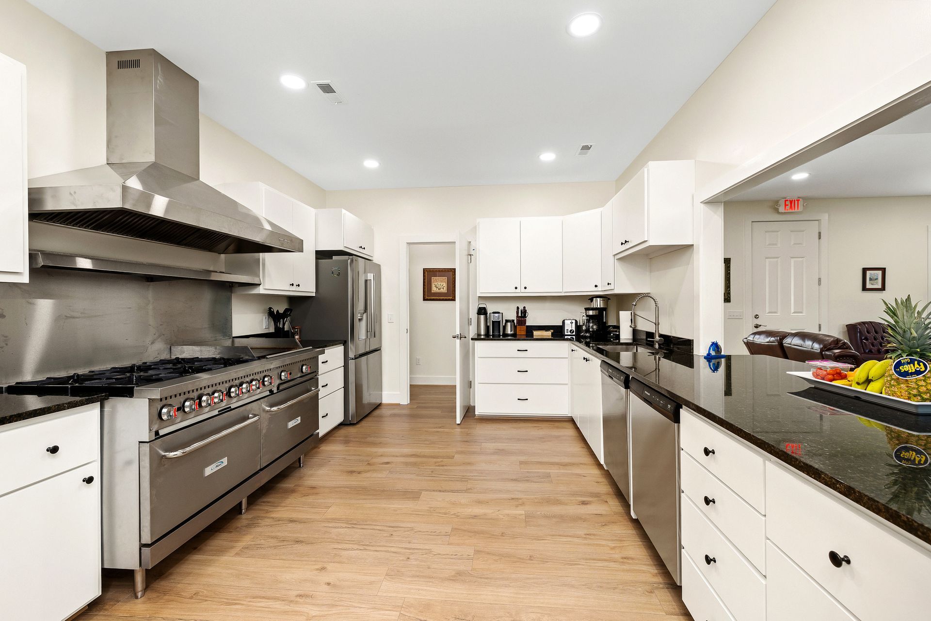 Spacious, modern kitchen with stainless steel appliances, white cabinets, and black countertops. The room has wood flooring and is brightly lit.