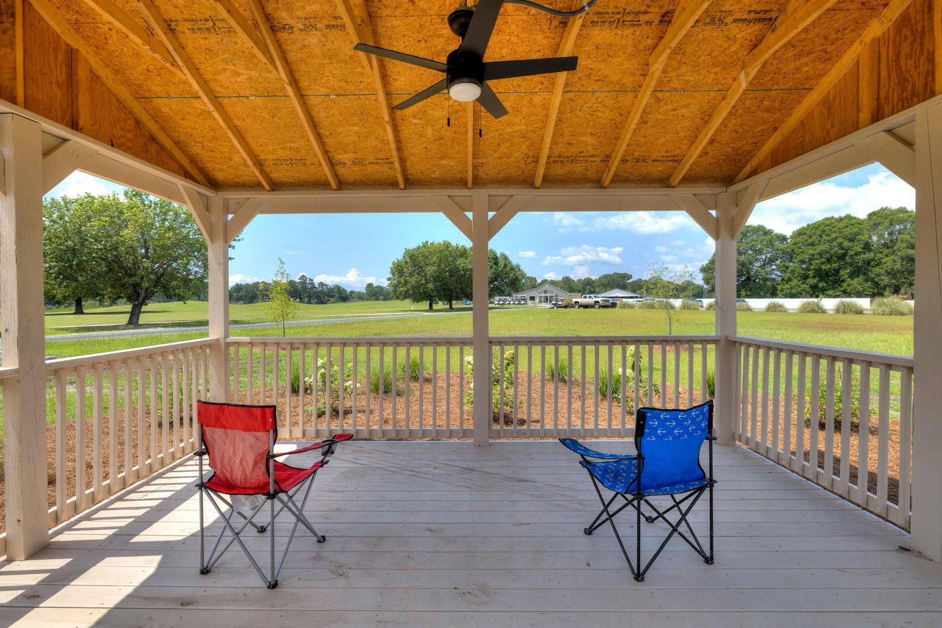 A gazebo overlooking a grassy field; two folding chairs sit inside.