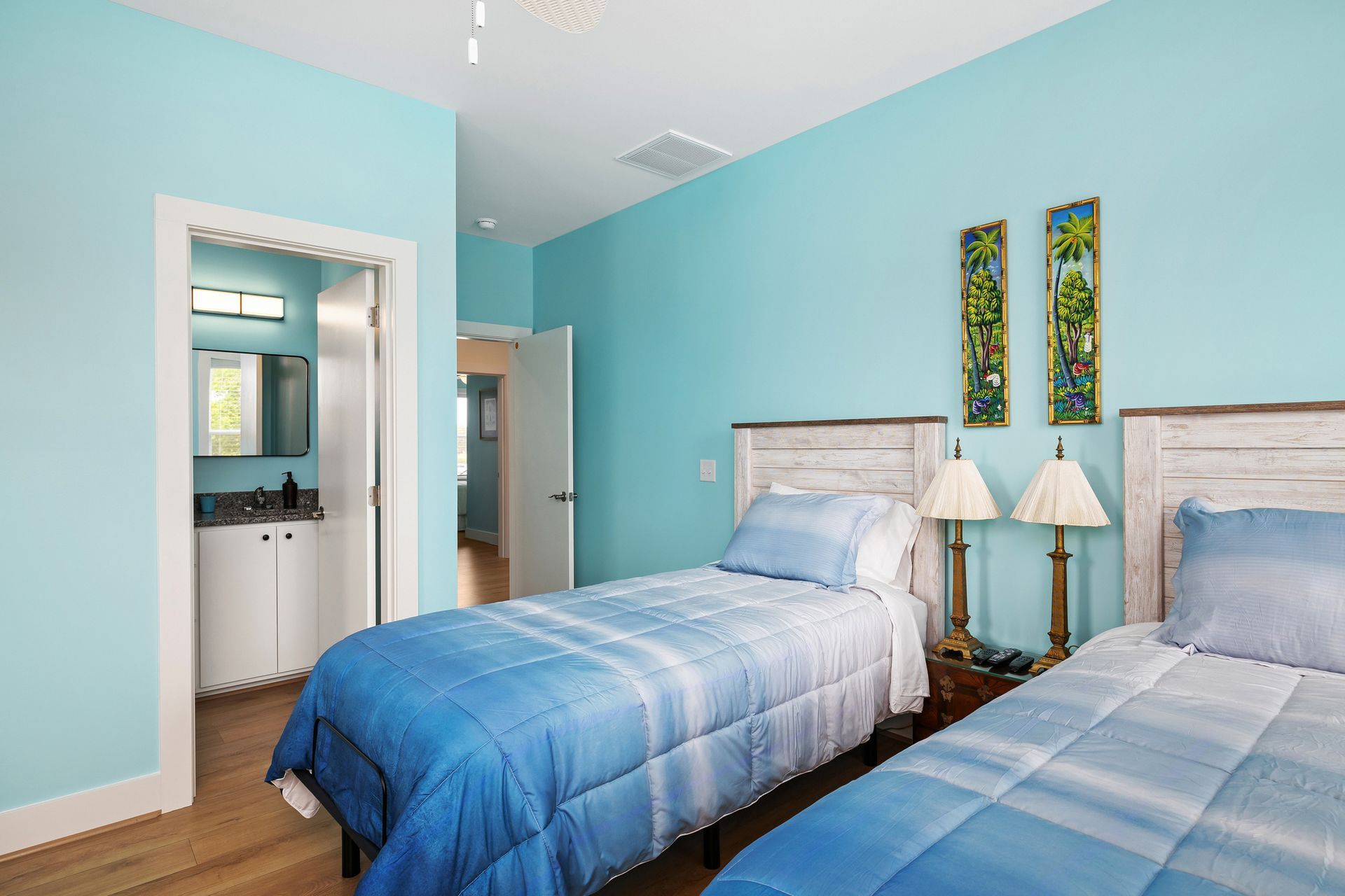 A bedroom with two twin beds, blue bedding, turquoise walls, and a bathroom in the doorway.