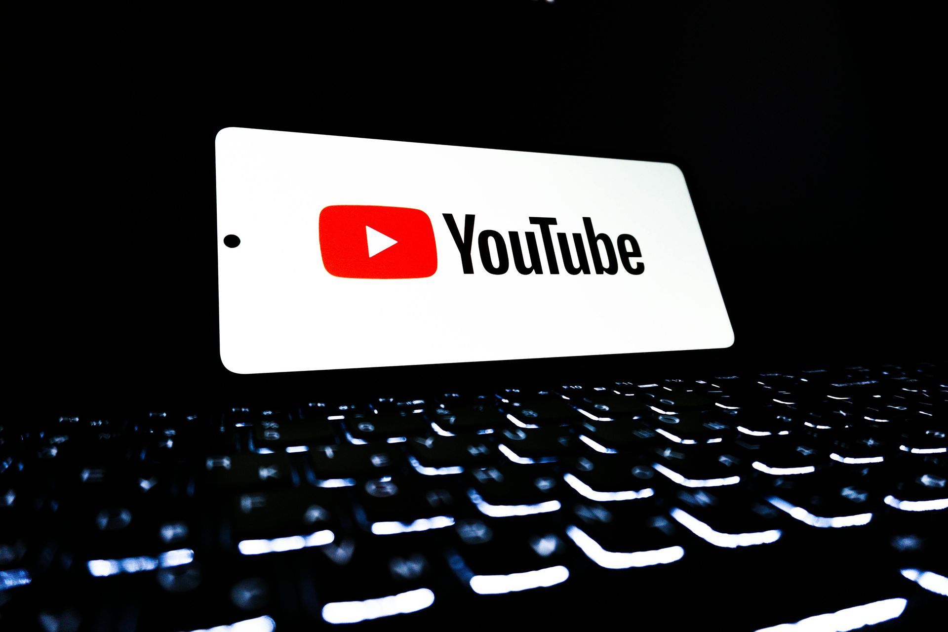 YouTube logo on a tablet screen above a backlit keyboard, set against a dark background.