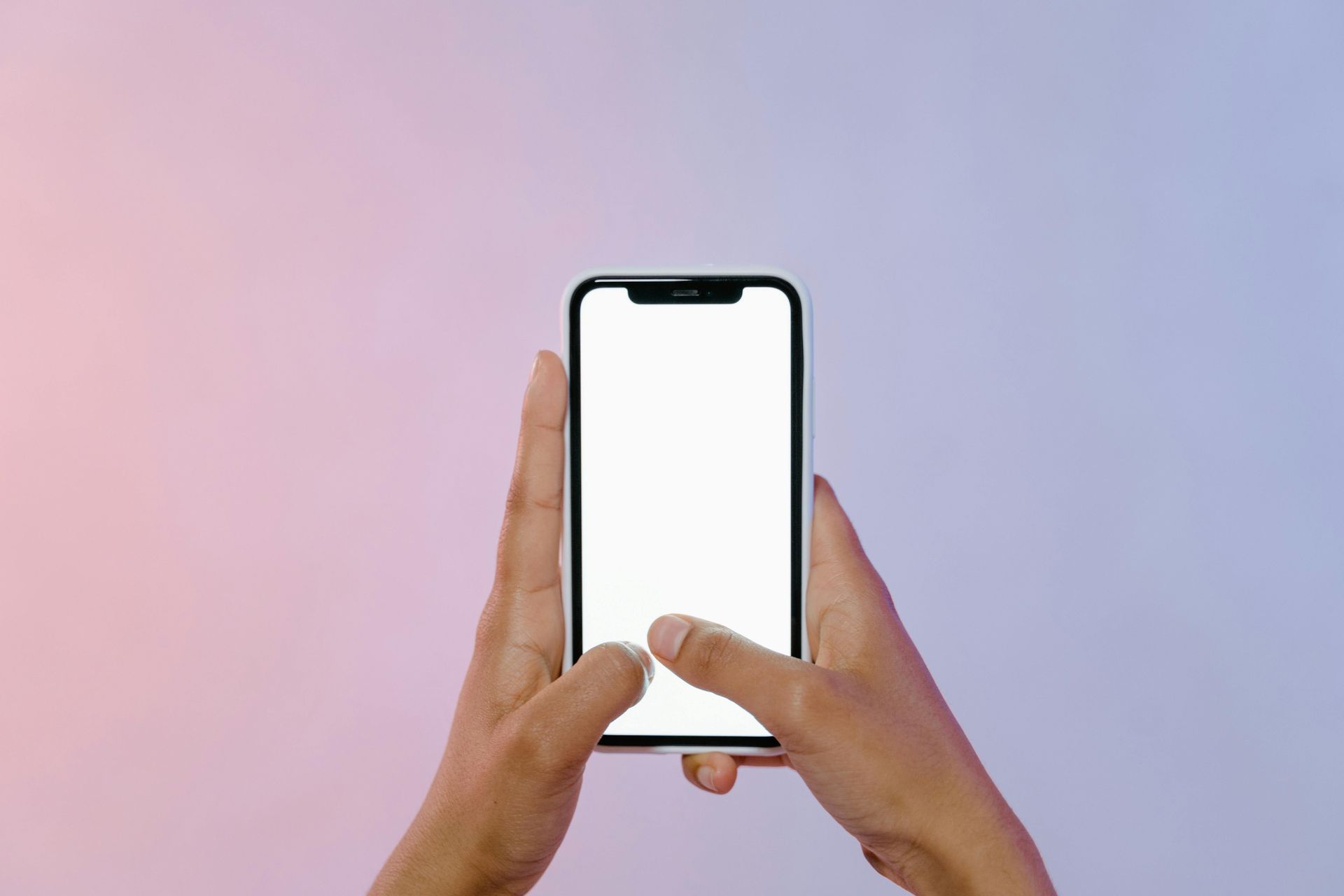 Hands holding a smartphone with a blank white screen against a gradient pink and blue background.