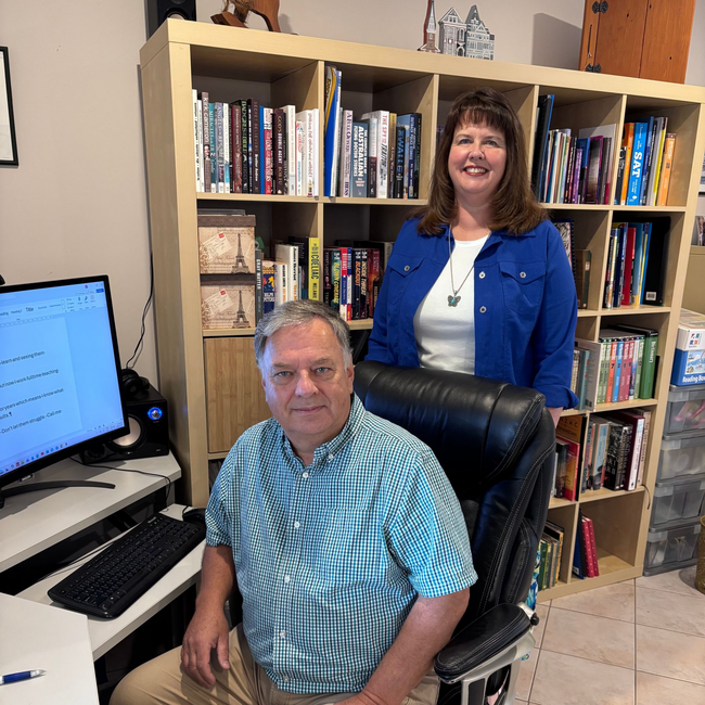 Two office workers, one seated and one standing, posing against a white background with colorful abstract accents