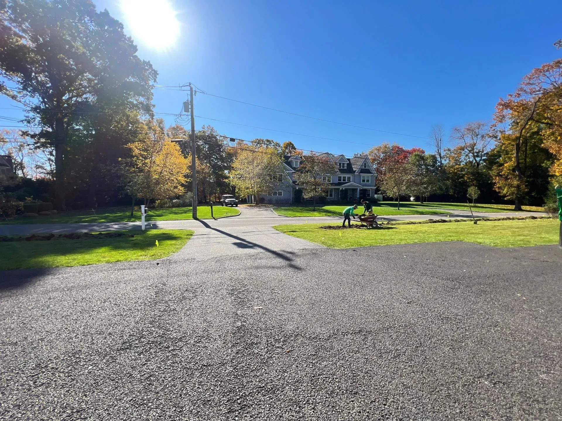 Gravel driveway leads to park with house in the background on a sunny day.
