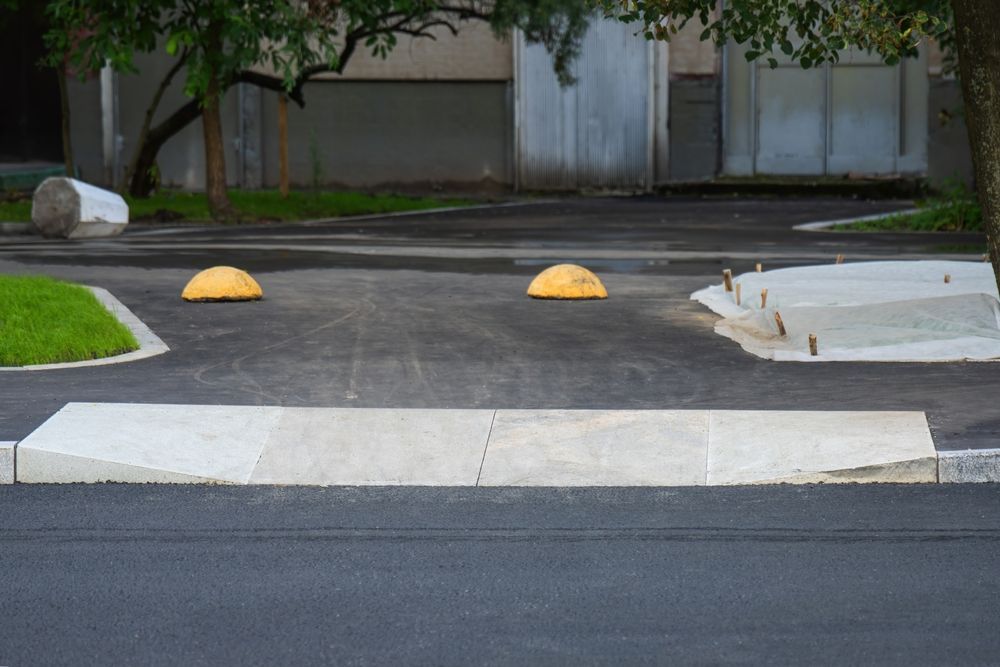 Asphalt driveway with two yellow parking bumpers and a concrete curb.