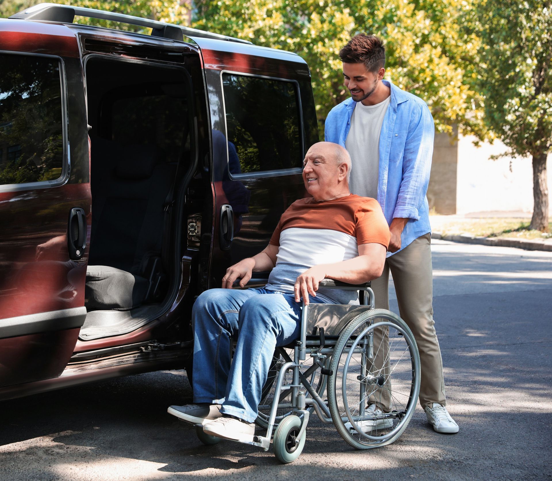 A person helping an individual in a wheelchair to enter a wheelchair-accessible van outdoors.