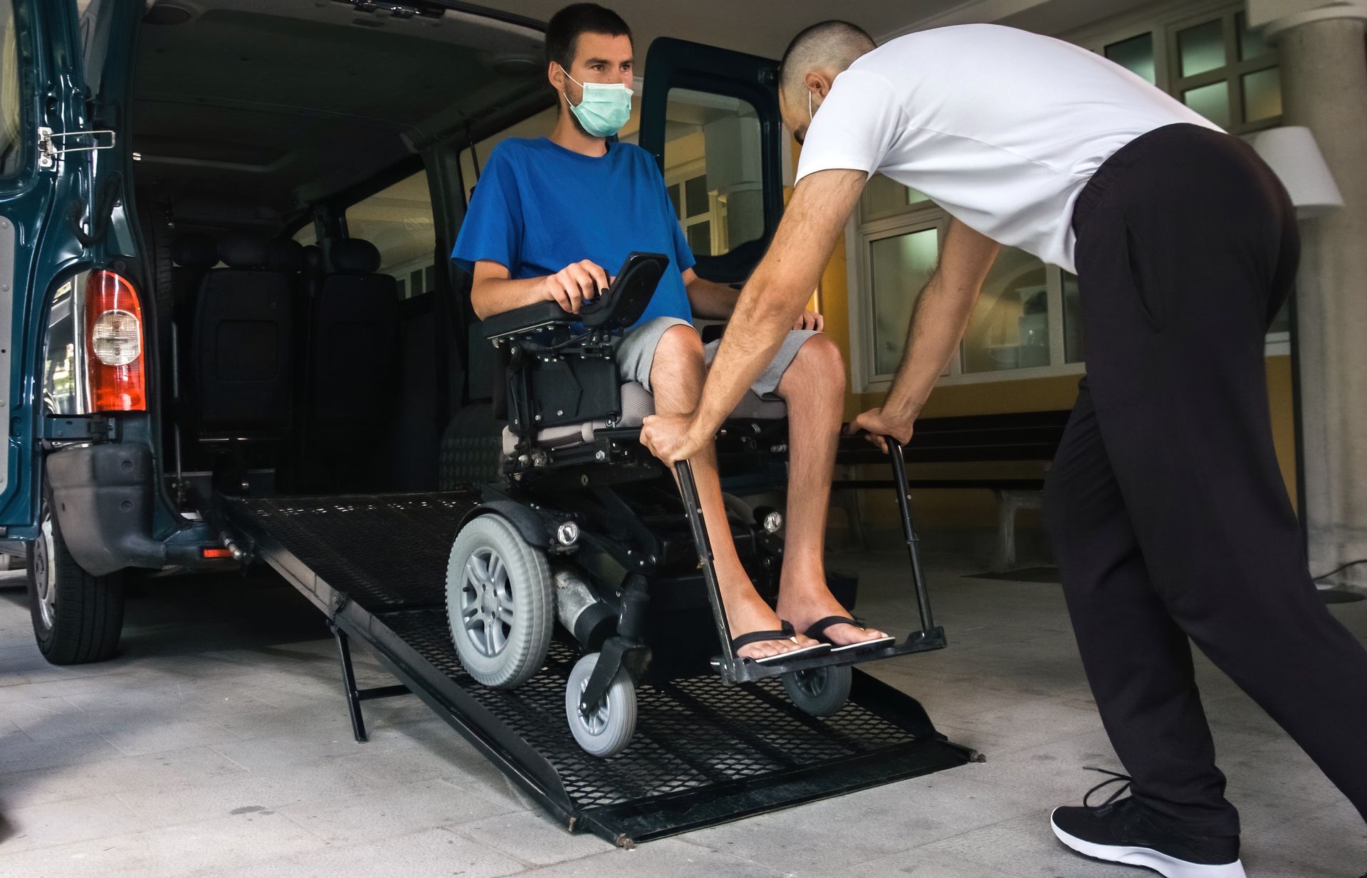 A person in a wheelchair is being assisted by another person to board a van via a ramp.