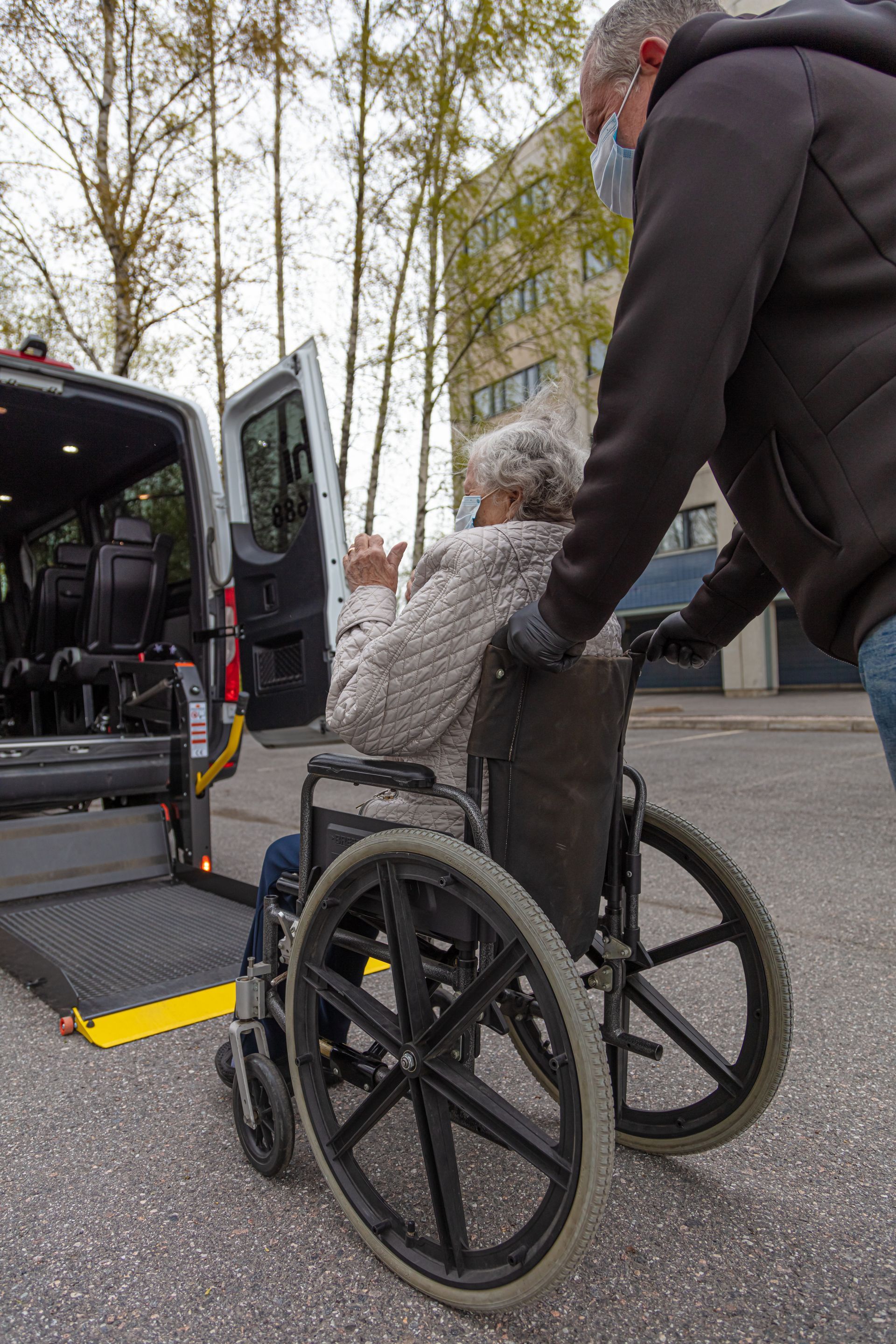 A person pushes another in a wheelchair toward a van with an extended ramp.