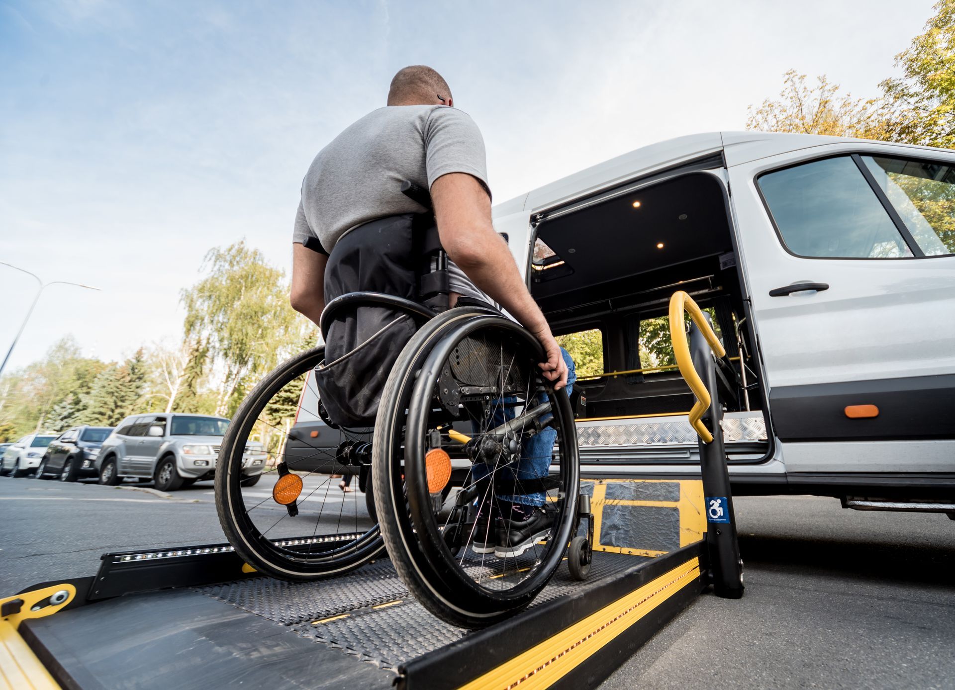 A person in a manual wheelchair using a lift to enter an accessible van parked on a street.