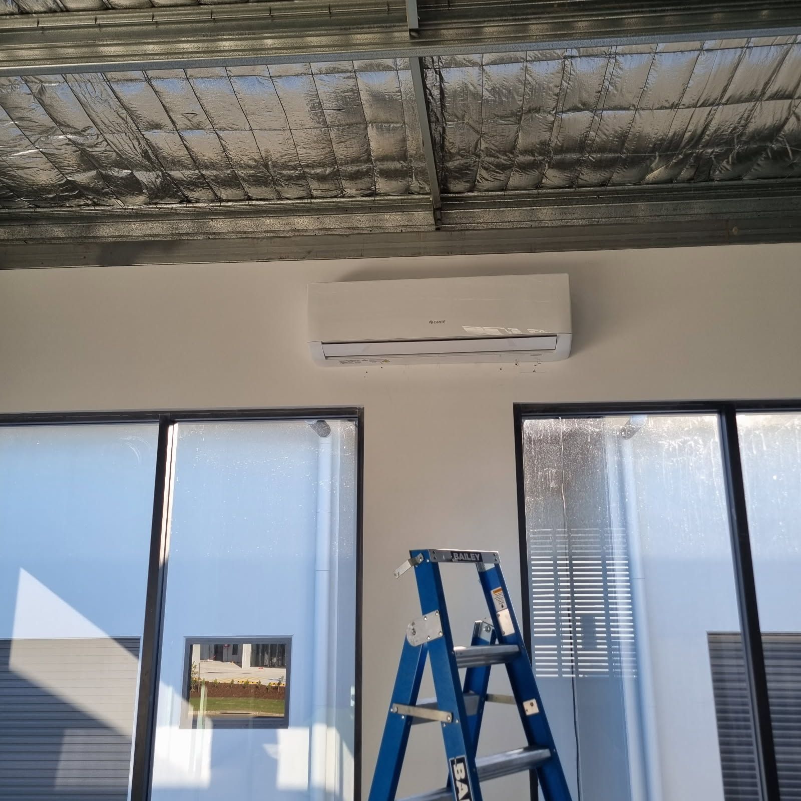 A Man Is Working On An Air Conditioner Outside Of A Building — Derek Knust Electrical In Mons, QLD