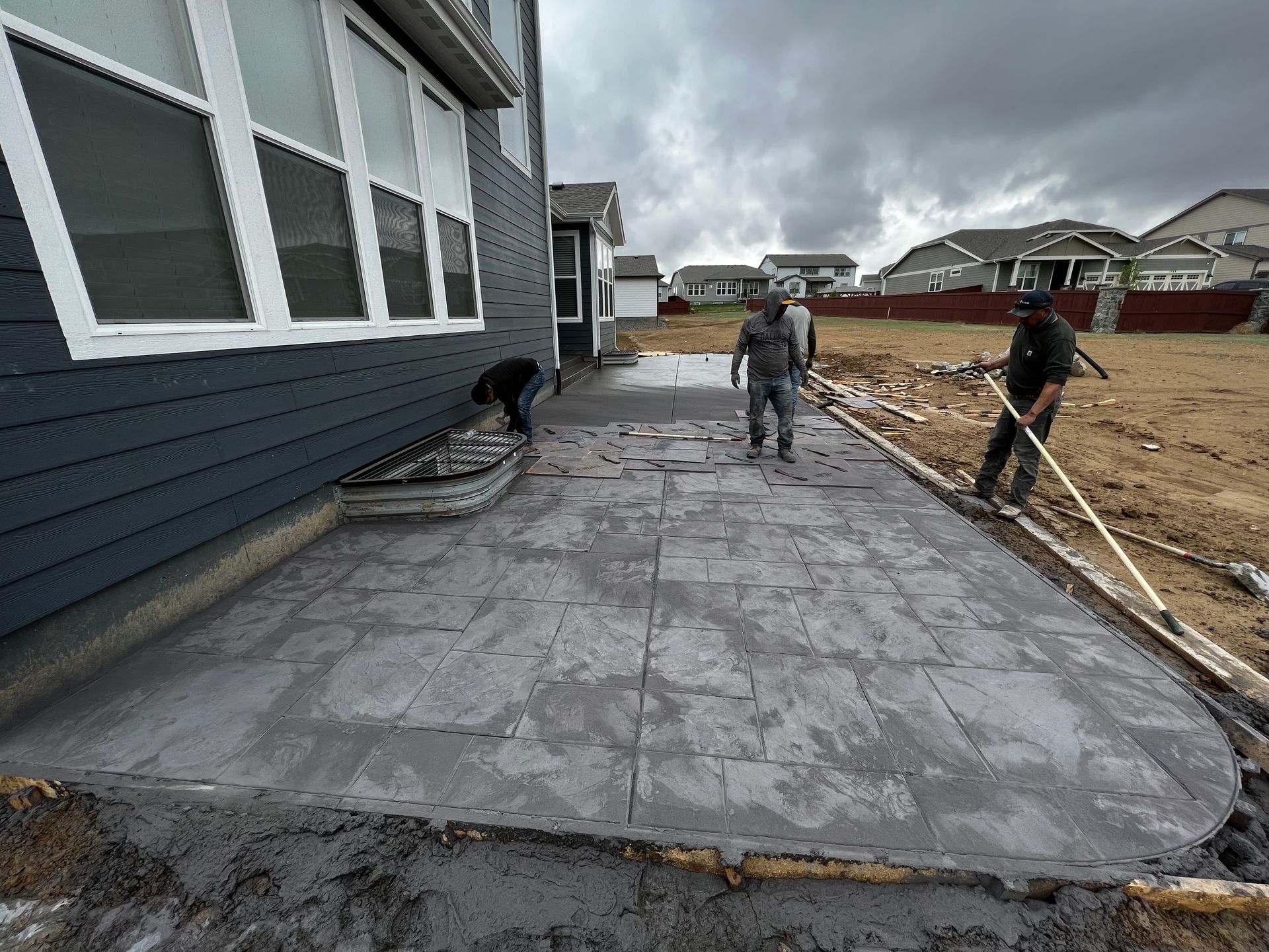 Two men are working on a concrete walkway in front of a house.