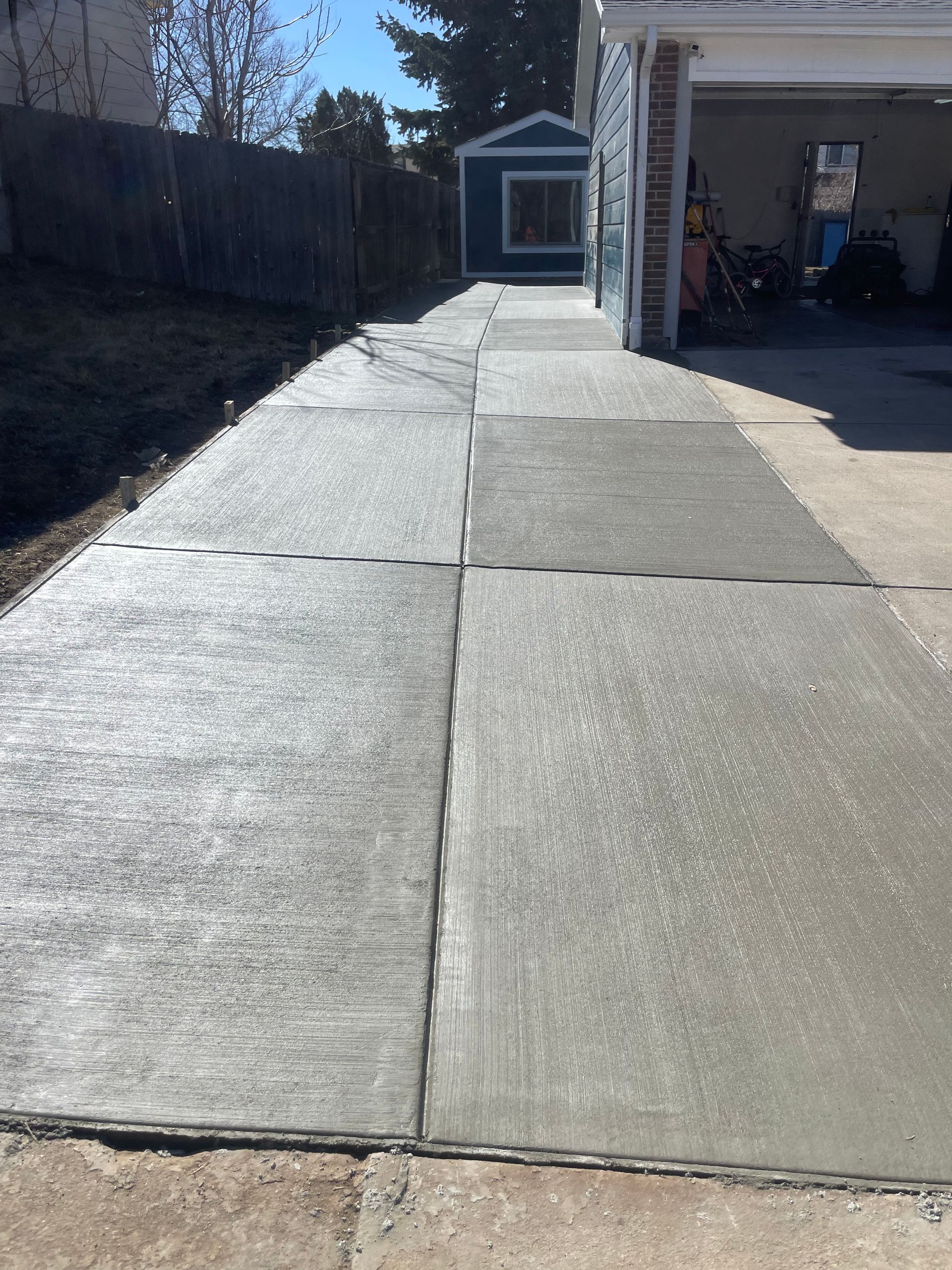 A concrete walkway leading to a garage with a blue shed in the background