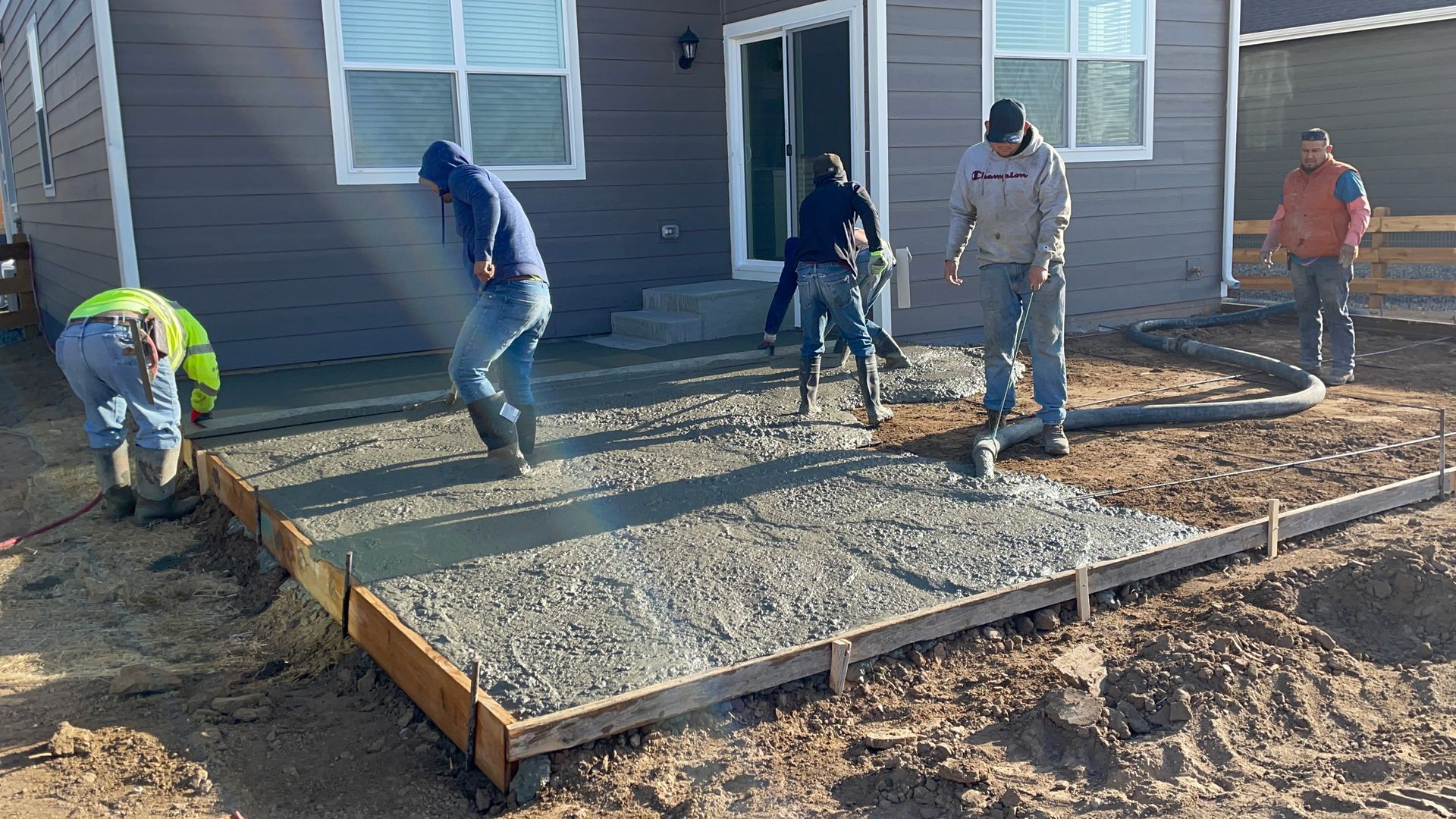 A group of construction workers are working on a concrete patio in front of a house.