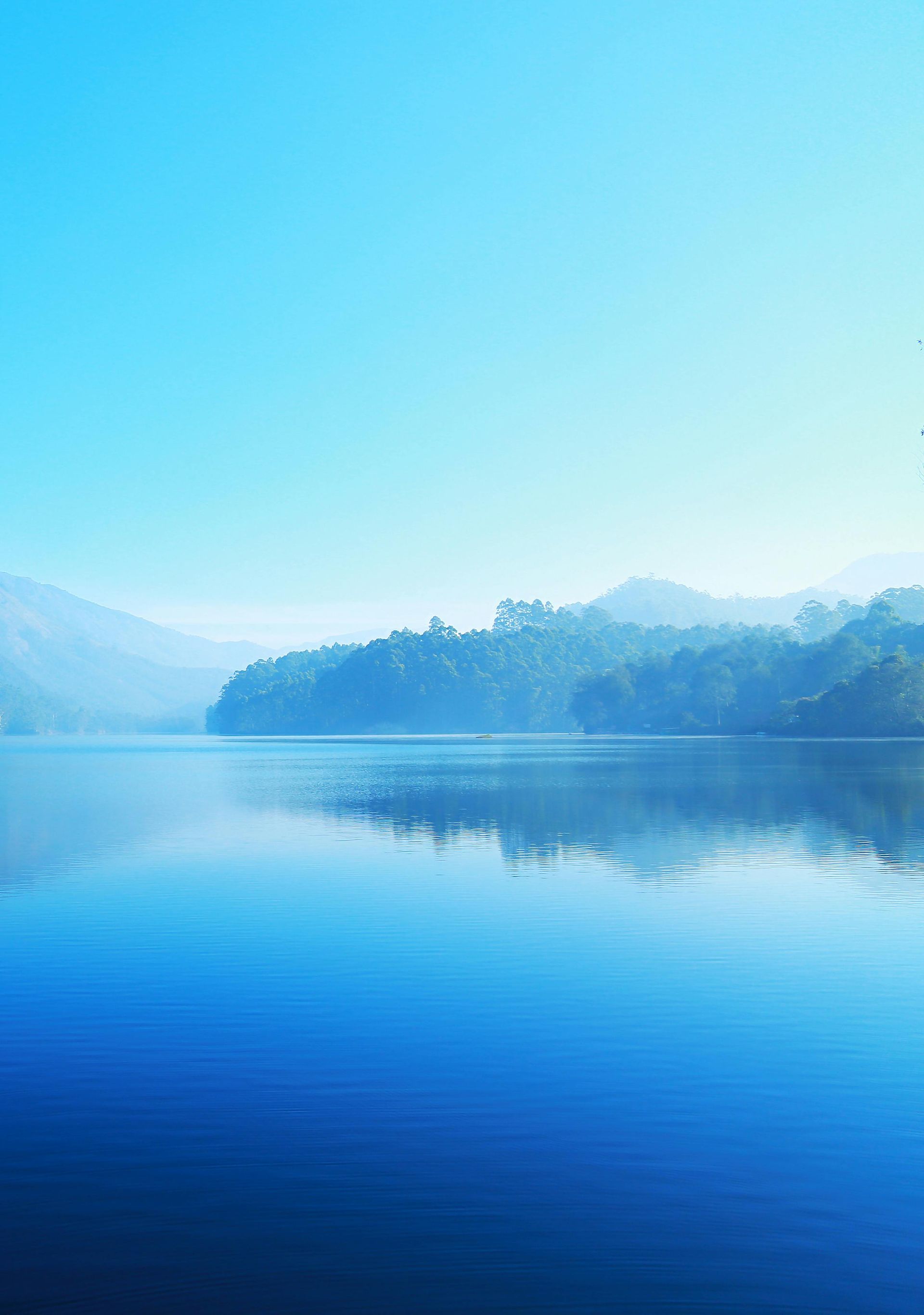 Blue lake reflecting the clear sky and distant hills with trees.