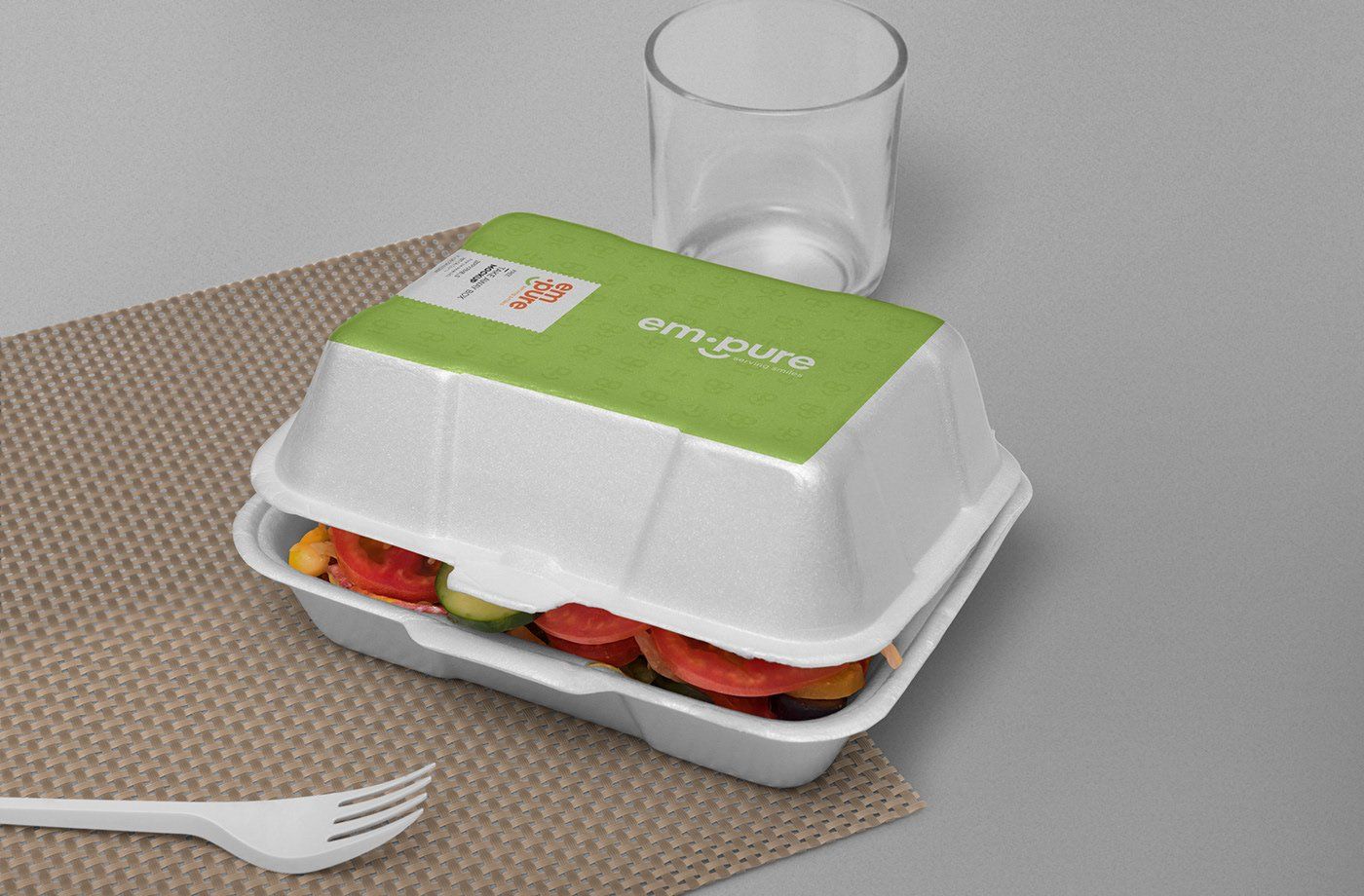 A styrofoam container filled with fruit next to a glass