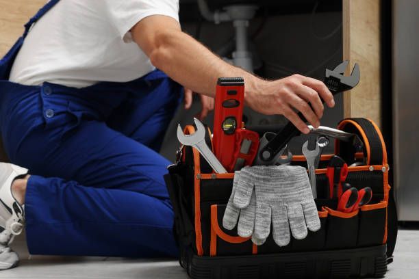 Close-up of a plumber in a blue and white uniform, taking an adjustable wrench from a tool bag.