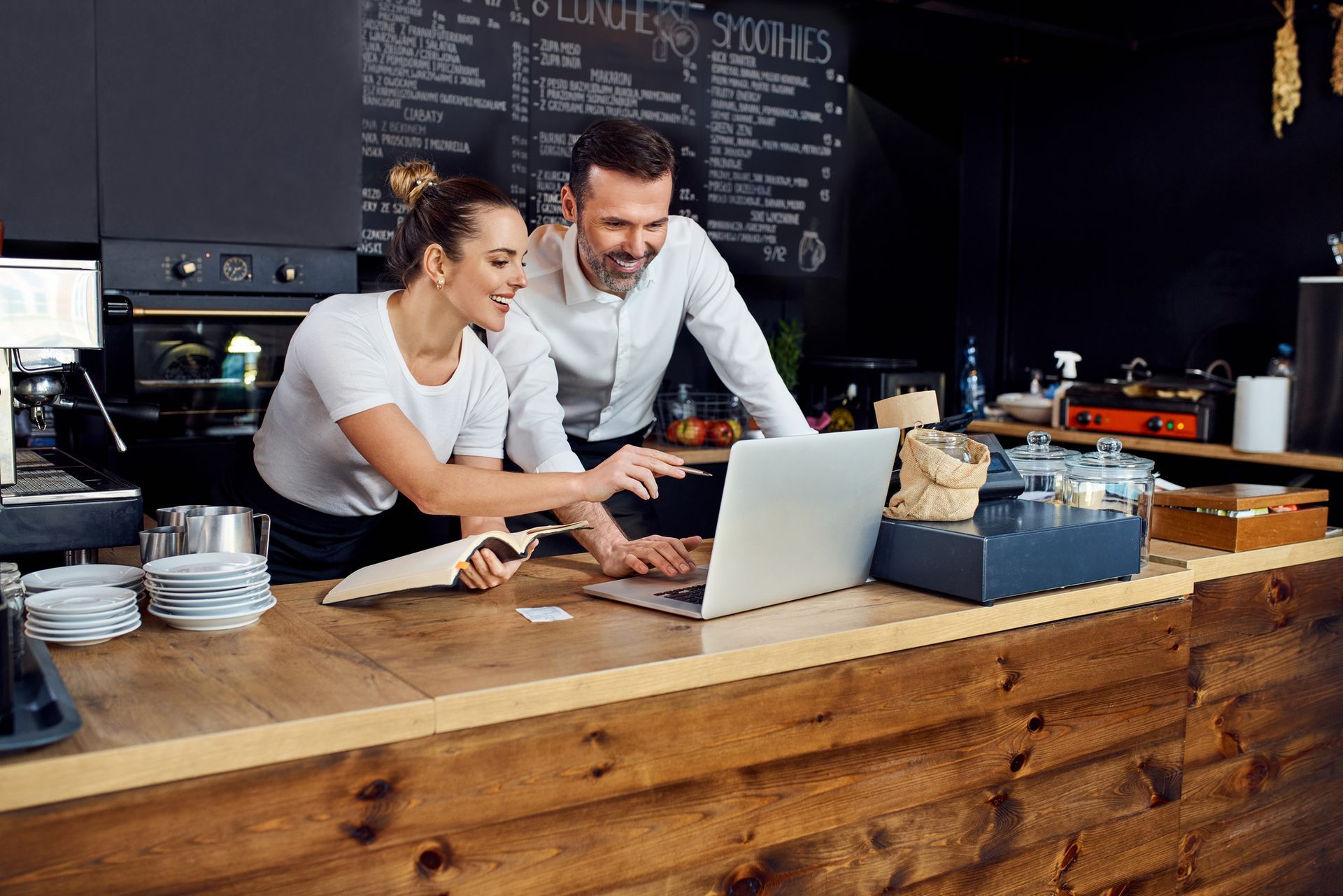 A man and a woman are looking at a laptop in a restaurant.